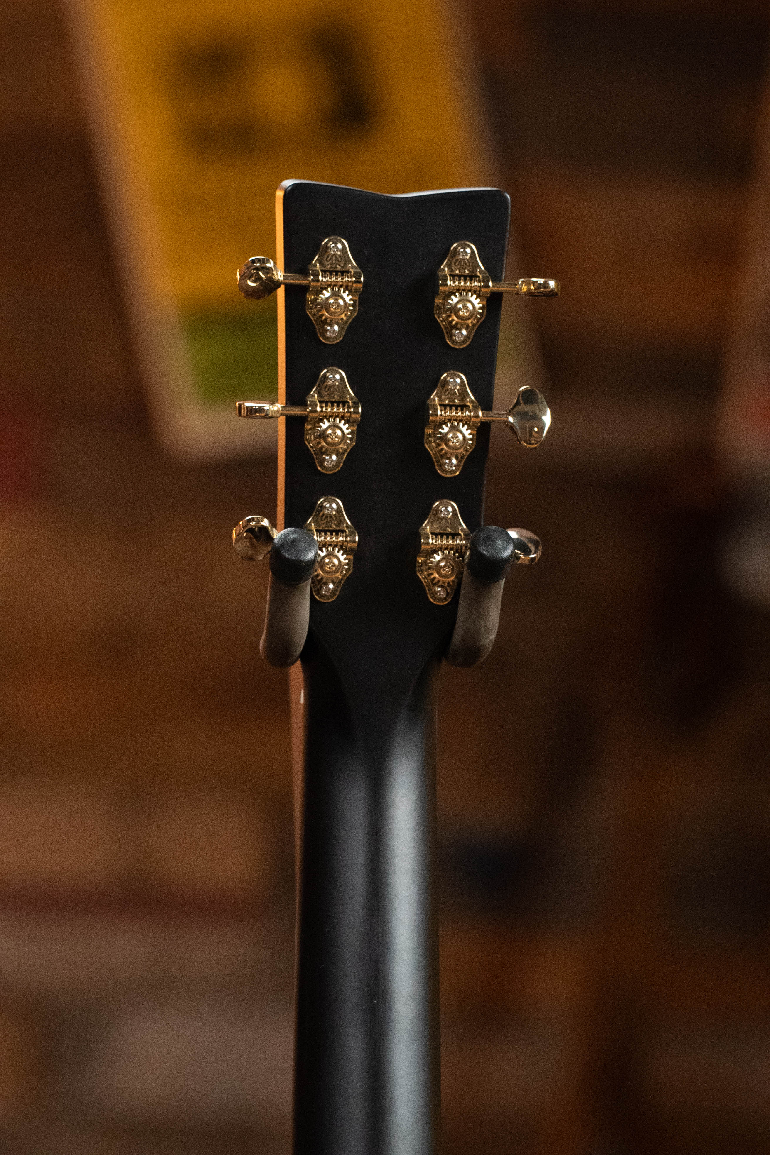 Close-up of the Yamaha TAG3C-SDB Sitka/Mahogany Sandburst Dreadnought Guitar’s headstock with gold tuners, on a stand under warm light. The newest TransAcoustic System enhances this Yamaha model’s appeal.