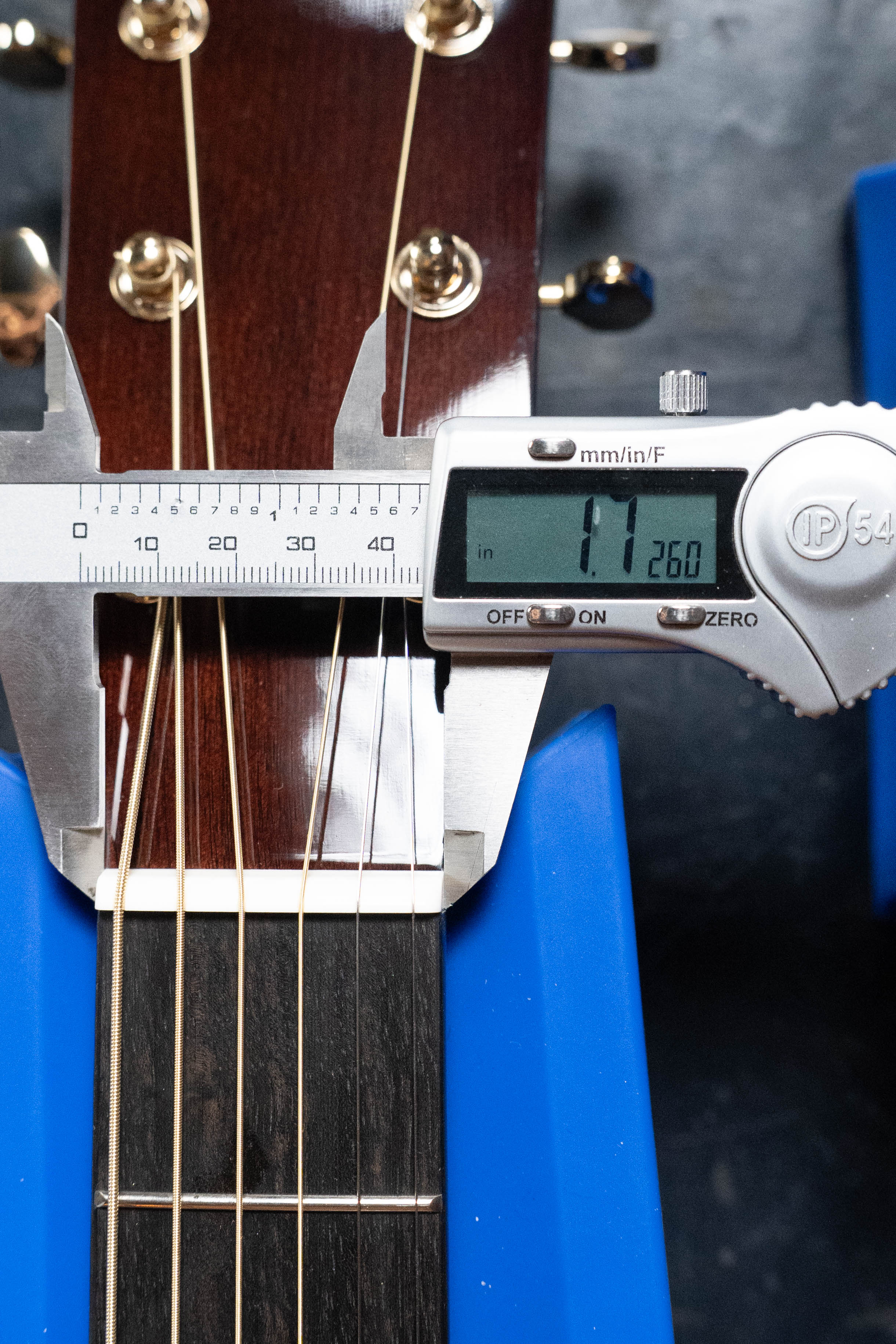 A digital caliper measures the Yamaha TAG3C-SDB guitar's neck width at the nut, displaying 1.260 inches. The guitar rests in a blue holder.