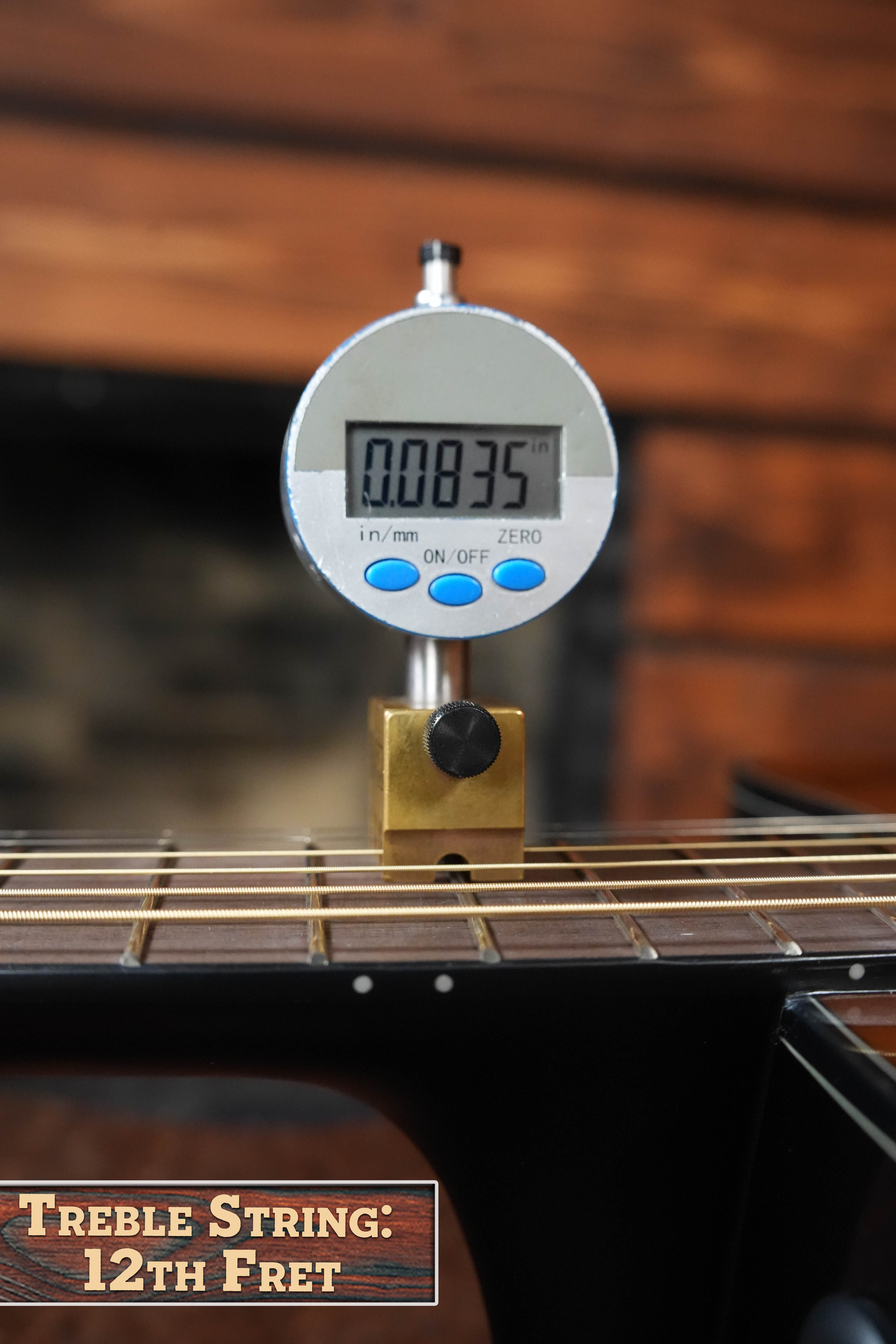 A digital gauge measures the treble string height at the 12th fret of a Yamaha TAS1 C Sitka/Mahogany Sand Burst Transacoustic Concert Guitar w/Cutaway #0132, displaying 0.0835 inches. A nearby sign reads: Treble String: 12th Fret.