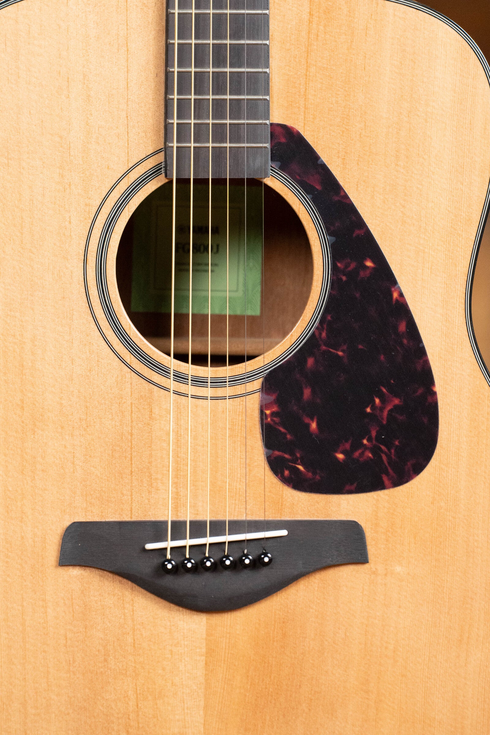 Close-up of a Yamaha GigMaker Deluxe Acoustic Pack - Natural Finish #8229 dreadnought body, highlighting its strings, sound hole, wooden bridge with black pins, and tortoiseshell-pattern pickguard on the light wood finish.