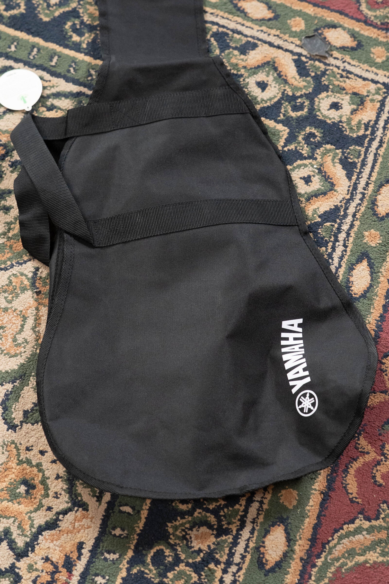 A Yamaha GigMaker Deluxe Acoustic Pack - Natural Finish #8229 gig bag in black rests on a patterned rug, featuring the Yamaha logo in white—perfect for your dreadnought guitar or acoustic guitar starter kit.