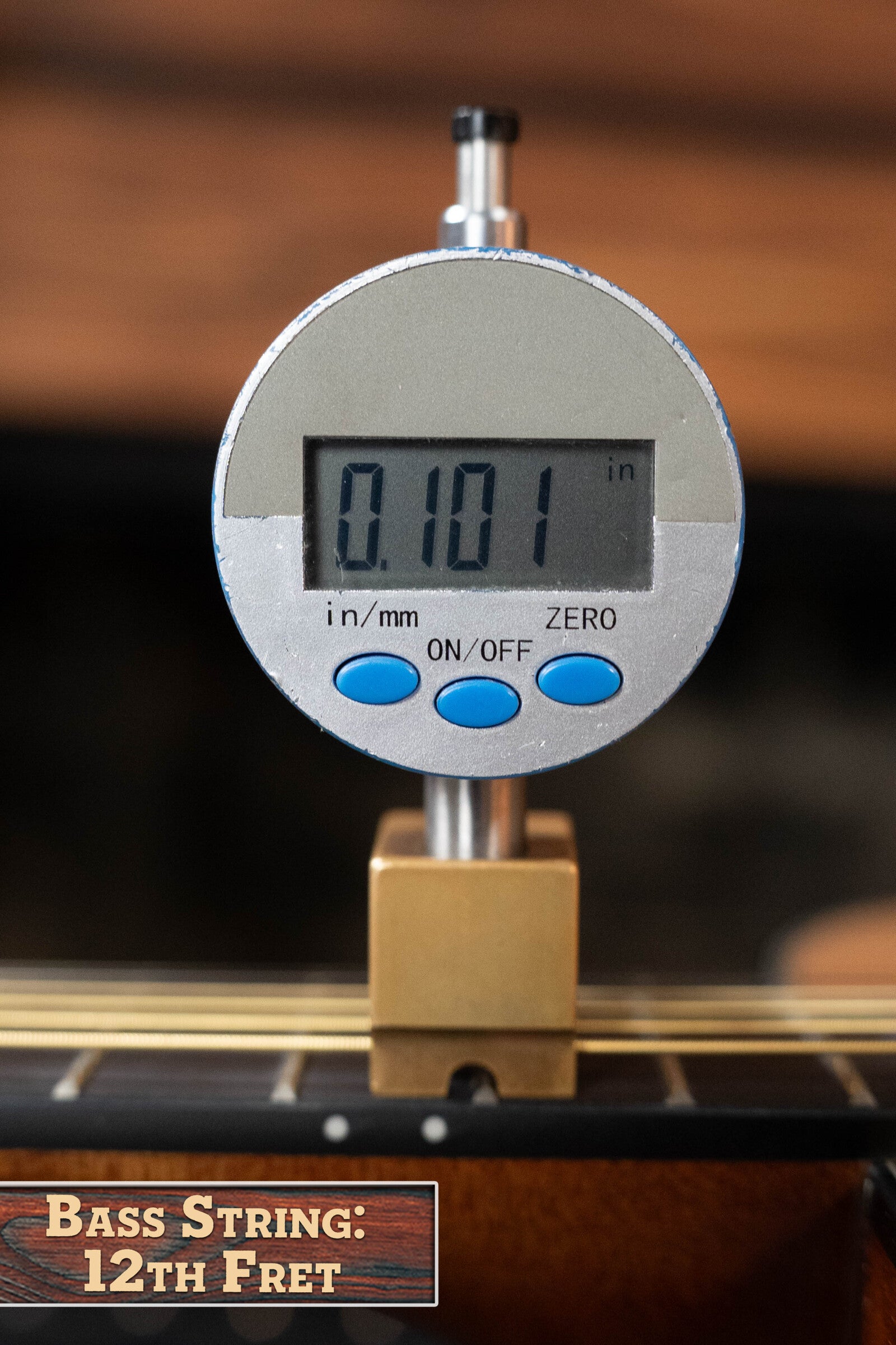 A digital gauge shows 0.101 inches while measuring bass string height at the 12th fret—ideal for setup comparisons with the Yamaha GigMaker Deluxe Acoustic Pack - Natural Finish #8229 by Yamaha.