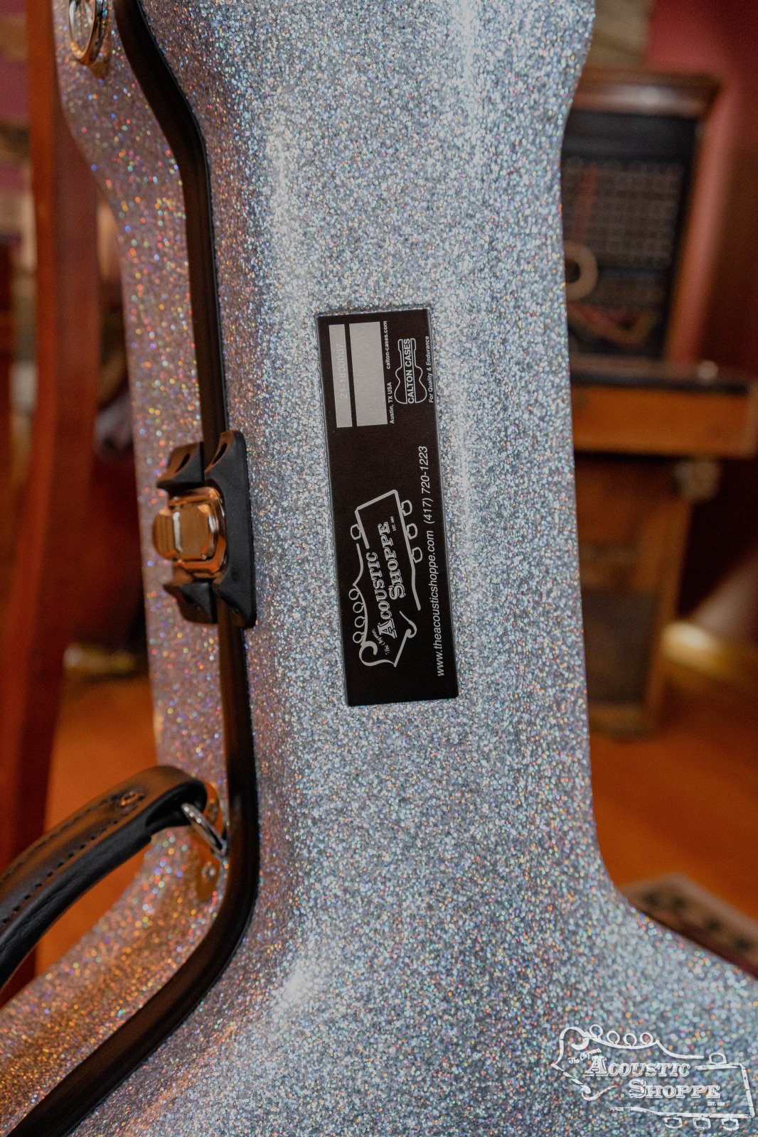 A close-up of a Calton Cases Dreadnought D-18 Diamond guitar case with a silver glitter exterior, black handle and latch, and a rectangular label reading Calton Cases and Big Sky Fest Acoustic Shoppe.