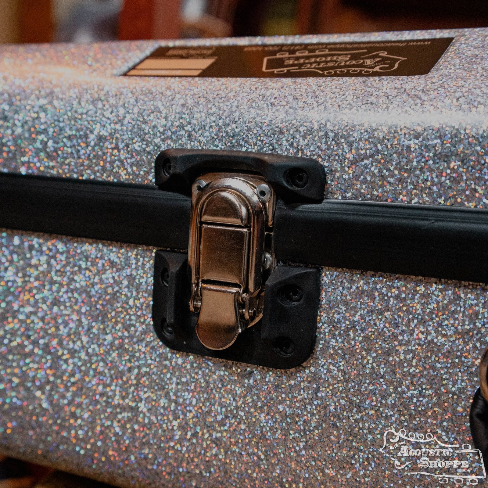 A close-up of the Calton Dreadnought D-18 Diamond Smooth Glitter case by Calton Cases, featuring a silver glitter exterior, shiny metal latch, black trim, and a sticker referencing the Acoustic Shoppe.