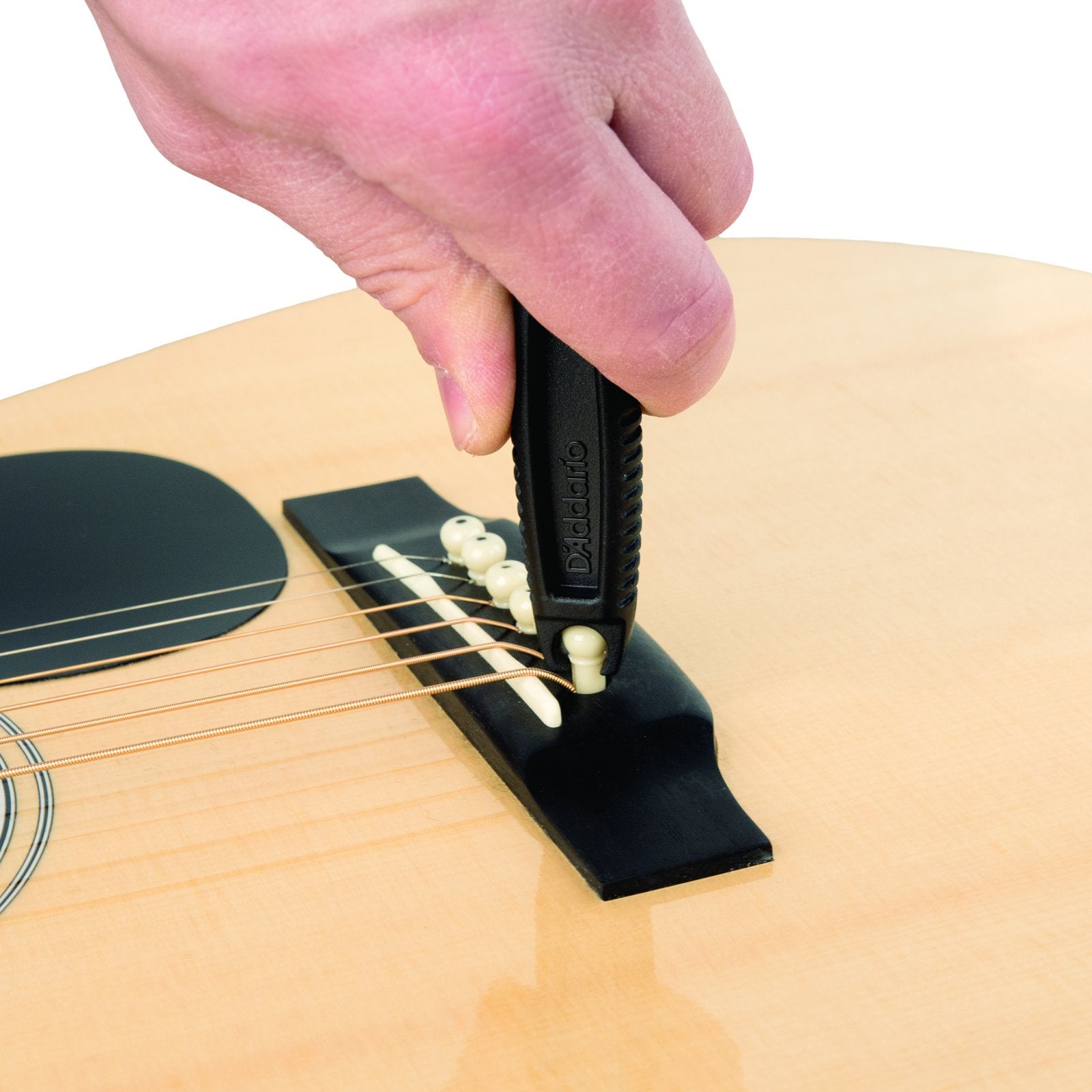 A hand uses the D'Addario Pro-Winder String Winder and Cutter (Black), a handy restringing tool, to remove a bridge pin from an acoustic guitar while changing strings.