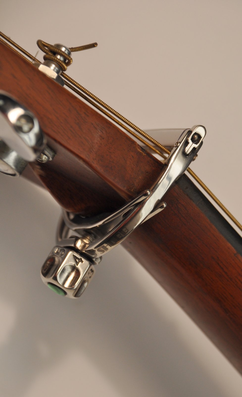 Close-up of a guitar neck with a Shubb F1 FineTune Screw-Operated Guitar Capo by Shubb clamped on the fretboard, designed for steel string guitars, set against a neutral background.