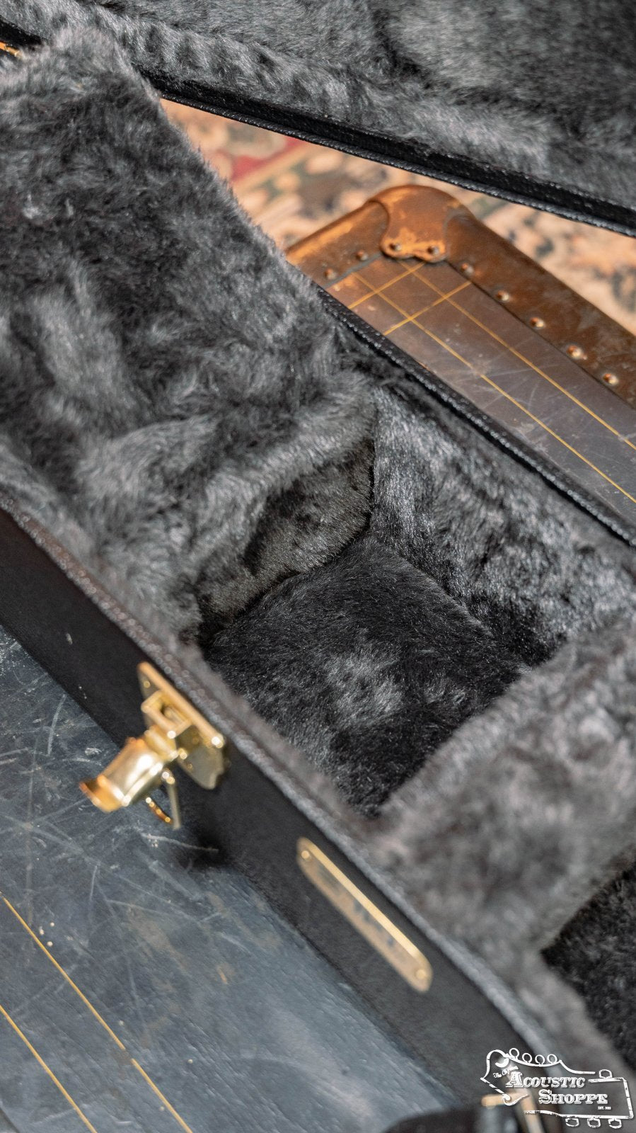 The TKL 7820 Premier Jumbo 6/12 String Hardshell Guitar Case by TKL, featuring a plush black interior and gold latch, is displayed open on a dark, subtly patterned surface.