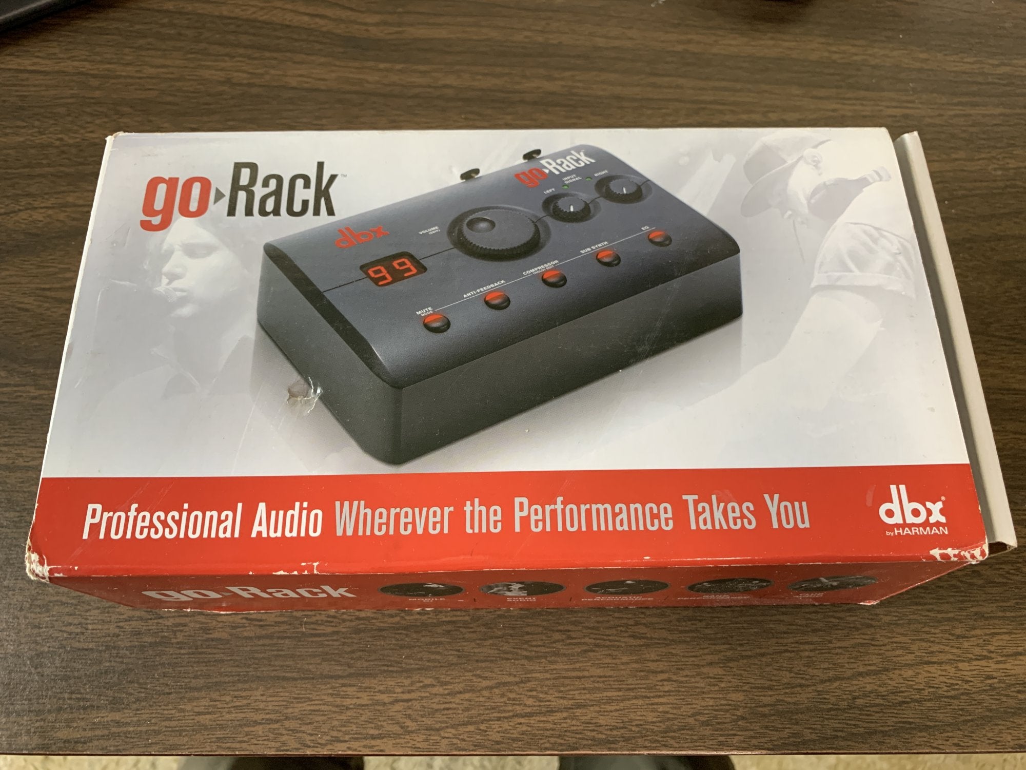 A boxed (Mint) DBX goRack Performance Processor by DBX rests on a wooden surface. The package shows the device and the slogan Professional Audio Wherever the Performance Takes You, perfect for PA system setups.
