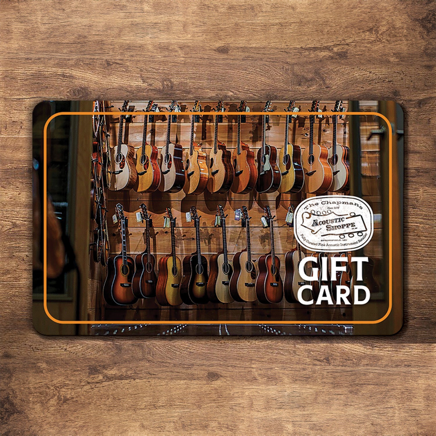 The Acoustic Shoppe Gift Card makes an ideal gift for music lovers, featuring acoustic guitars in a shop scene with "Gift Card" and The Acoustic Shoppe logo displayed on a wooden surface.