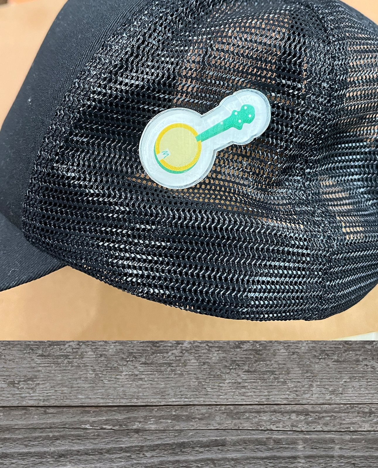 A Yellow Banjo Acrylic Lapel Pin by Mark A Montgomery sits on a wooden surface at an Eastman dealer specializing in acoustic instruments.