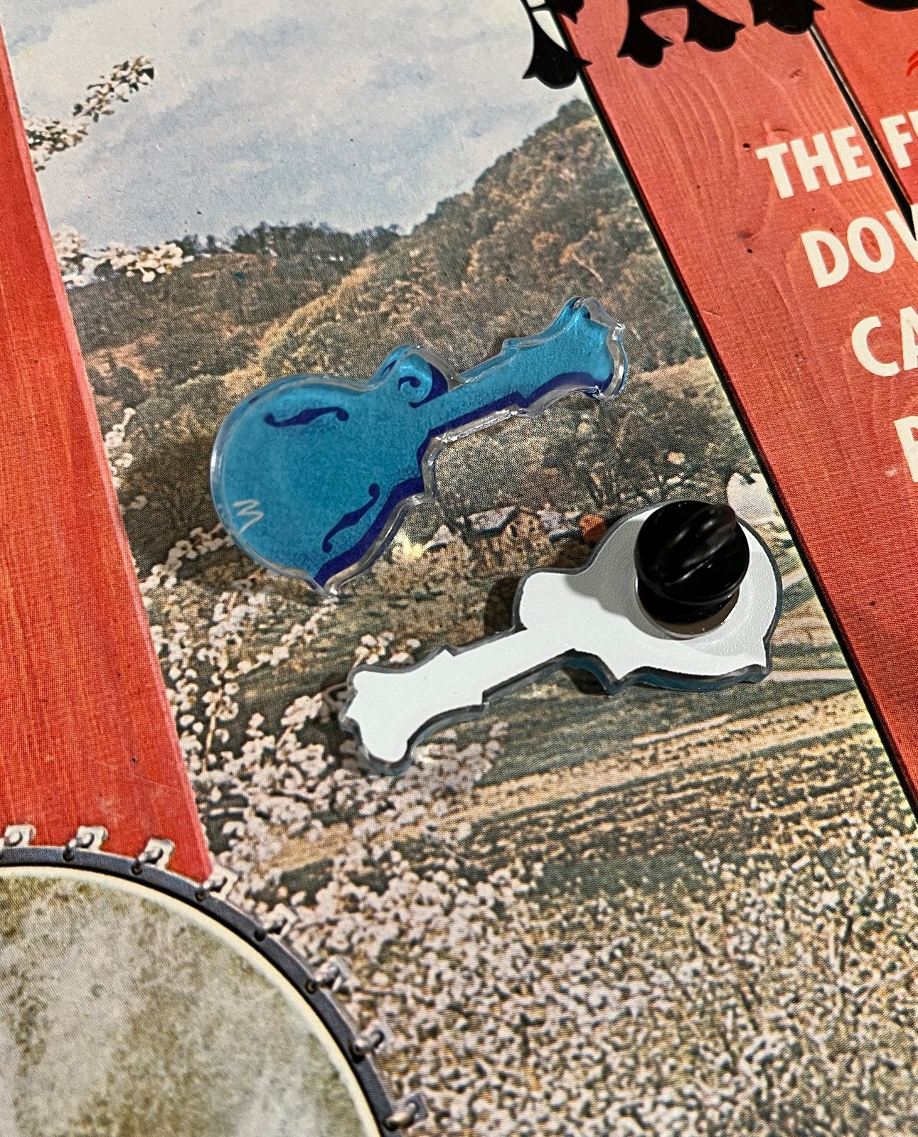 The Blue Mandolin Acrylic Lapel Pin by Mark A Montgomery is displayed on a vibrant background—ideal for collectors and fans of boutique instruments like those from Mark A Montgomery.