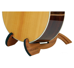 Close-up of the lower body of an acoustic guitar on a Cooperstand Pro-G Instrument Stand by Cooperstand, featuring curved supports and crafted from African Sapele hardwood, set against a white background.