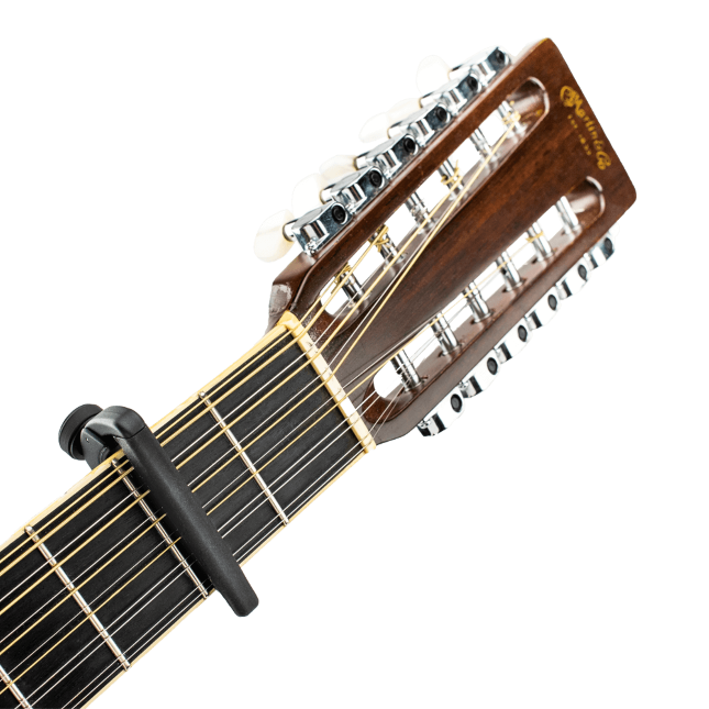 Close-up of a twelve-string acoustic guitar's headstock and upper neck with a black D'Addario Pro Plus Guitar Capo featuring FlexFit technology, tuning pegs, and part of the D'Addario brand name visible.