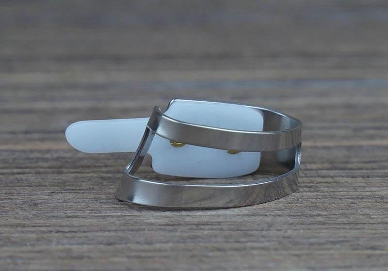 A close-up of the Deering Banjos ProPik Quik-Pik Thumb Pick Medium (11-206-3013), with a metal guard reminiscent of a knight’s visor, rests on wood—offering adjustable, precise control for musicians.