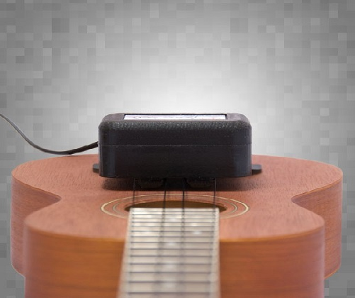 A close-up of a ukulele with a ToneRite Ukulele device from The Acoustic Shoppe attached to its soundhole, highlighting the play-in process against a gray, pixelated background.