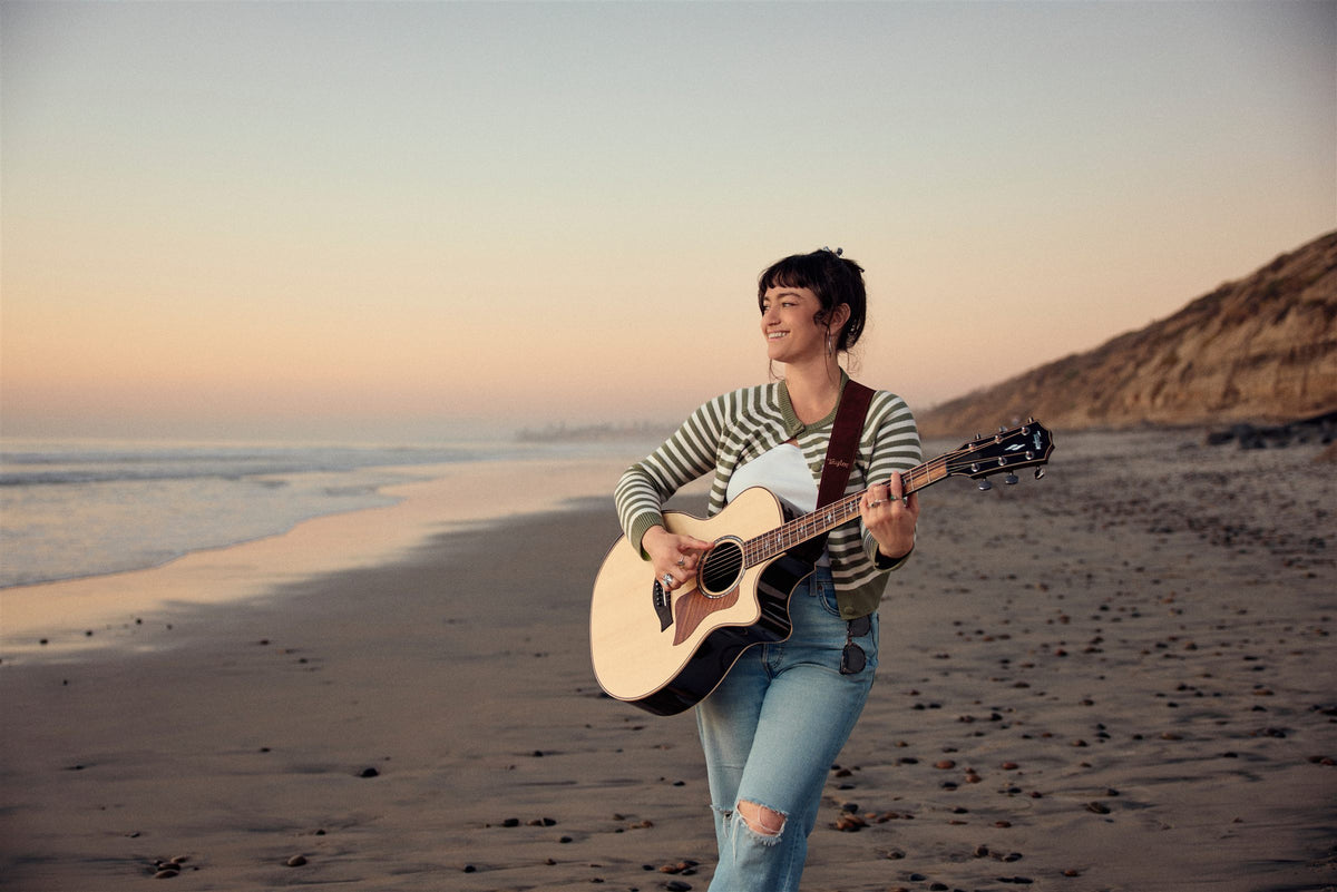 Taylor 800 Series lifestyle photo — musician playing a Taylor 814ce on the beach at sunset, The Acoustic Shoppe