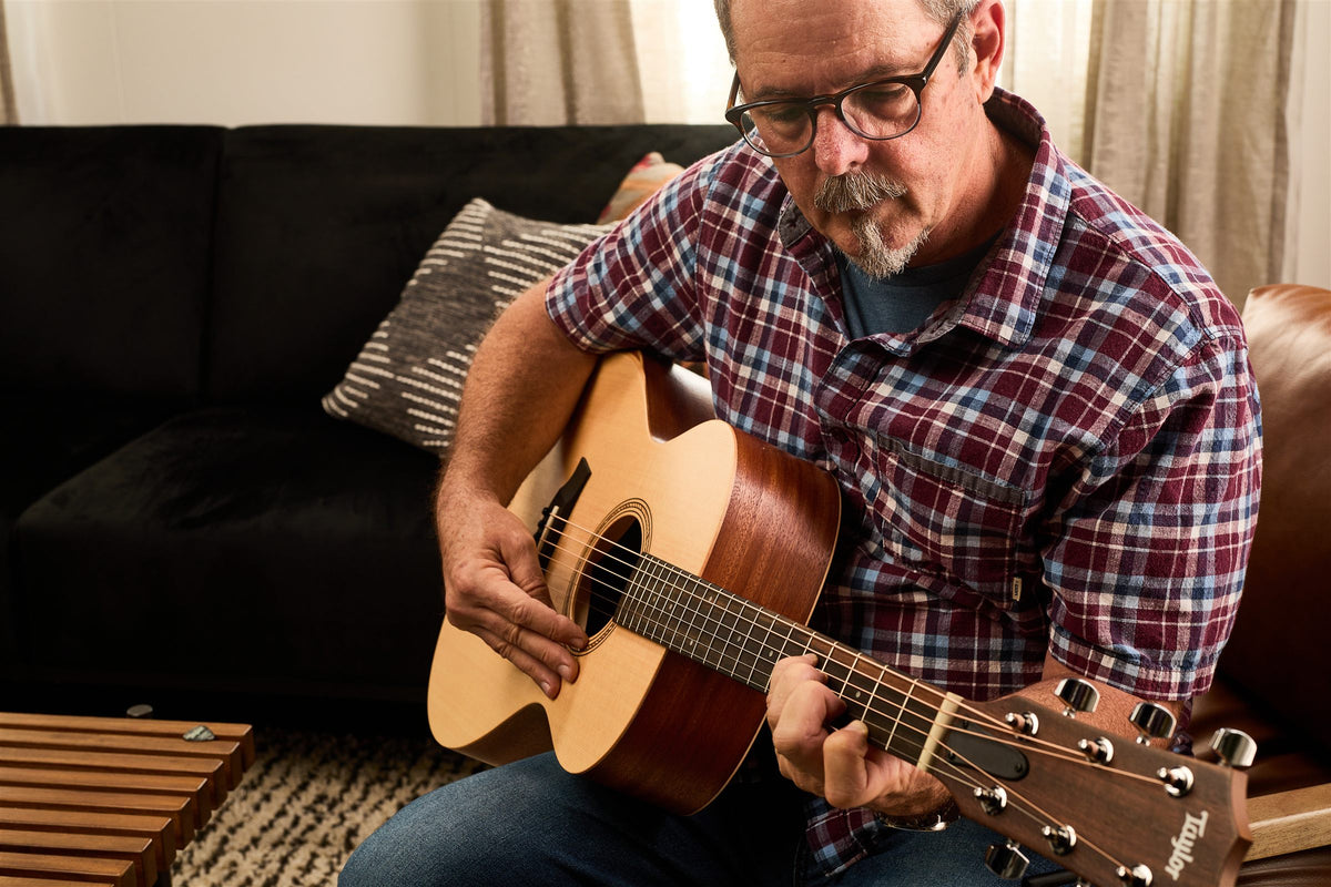 Taylor Academy lifestyle photo — musician playing an Academy 12e at home, The Acoustic Shoppe