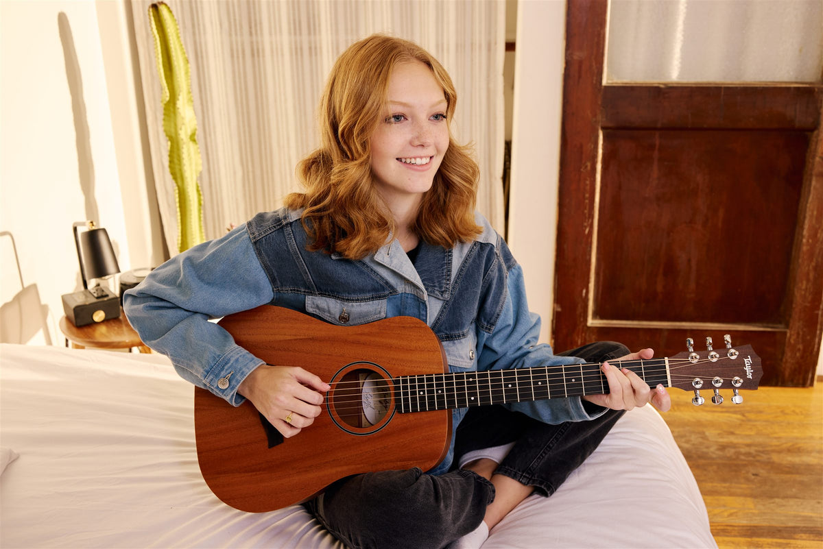 Baby Taylor lifestyle photo — young player with a Baby Taylor BT2 on a bed, The Acoustic Shoppe