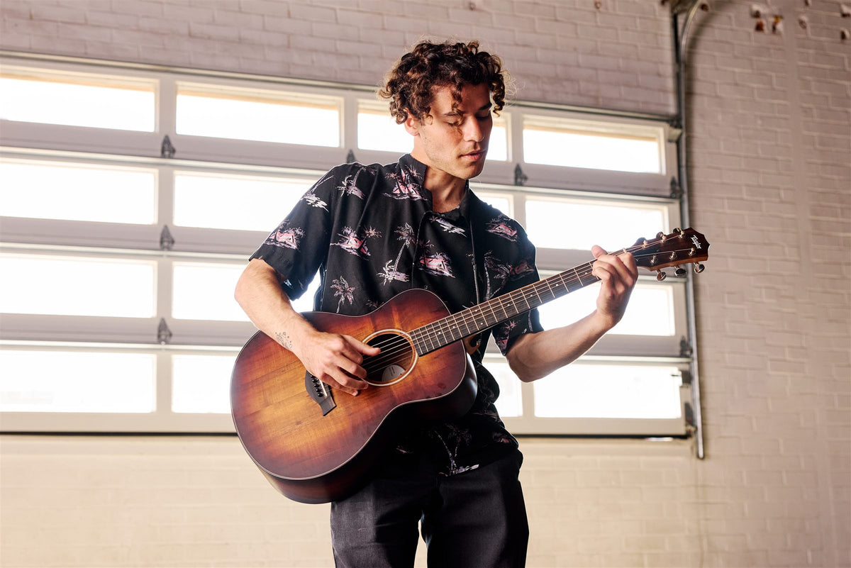 Taylor GS Mini lifestyle photo — musician playing a GS Mini-e Koa Plus in a garage studio, The Acoustic Shoppe