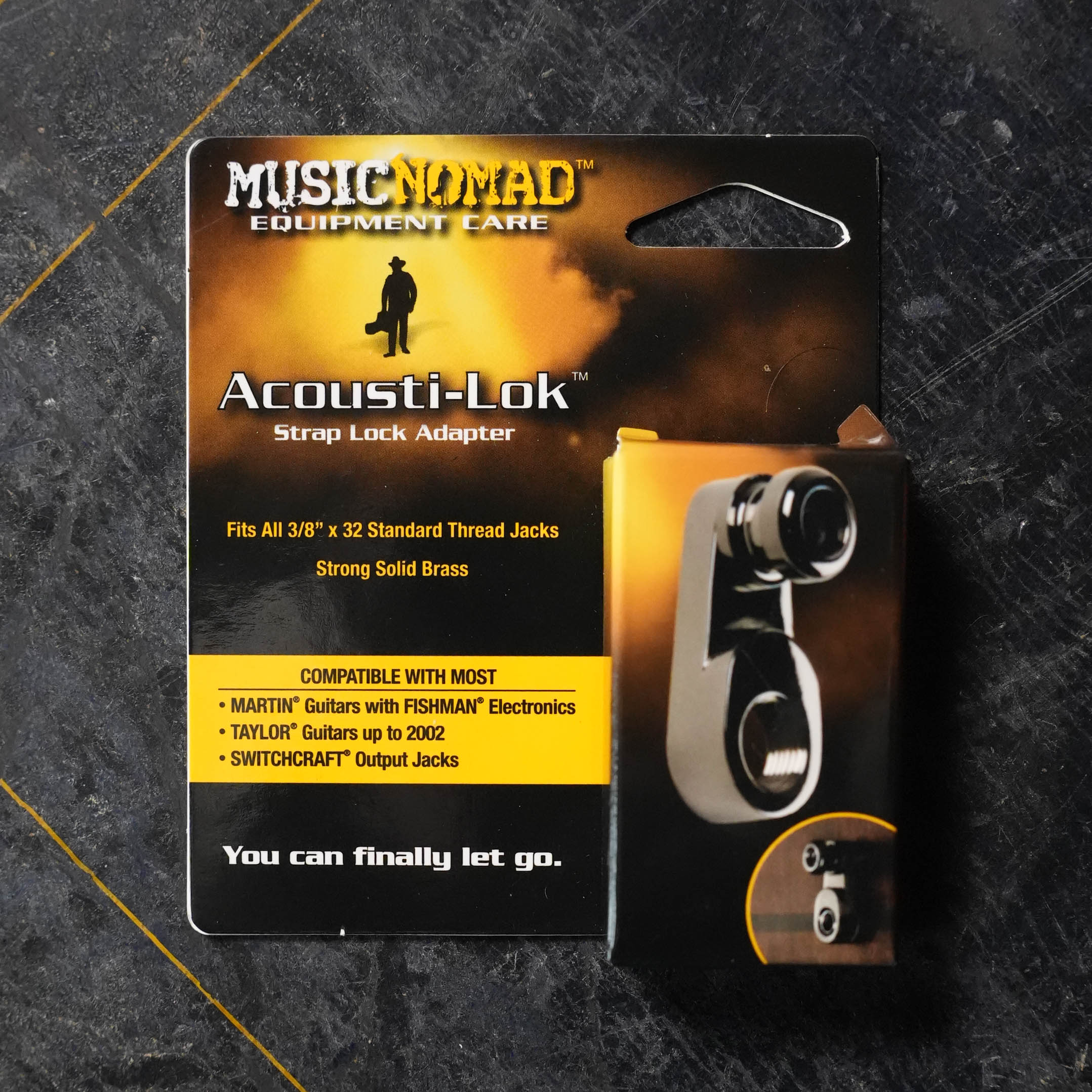Package of Music Nomad Acousti-Lok Strap Lock Adapter for Standard Output Jacks (MN270), compatible with various guitars. Black packaging with yellow and white text, featuring an image of the adapter on the right side.