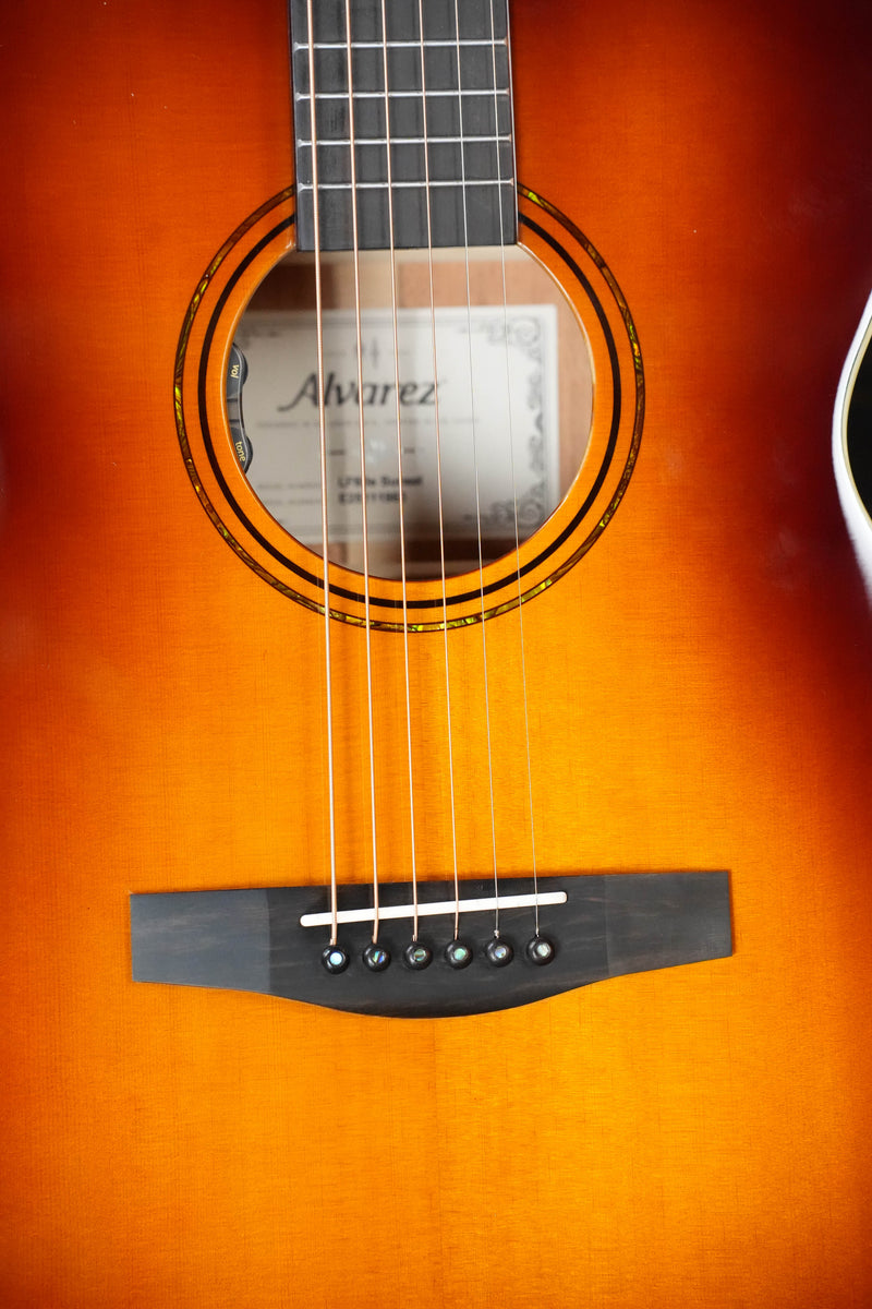 Close-up of the Alvarez Laureate Series LF60e Sunset Sitka/Mahogany OM Guitar, featuring strings, sound hole, bridge, sunburst finish, visible label inside, and enhanced acoustic resonance with an LR Baggs HiFi pickup.