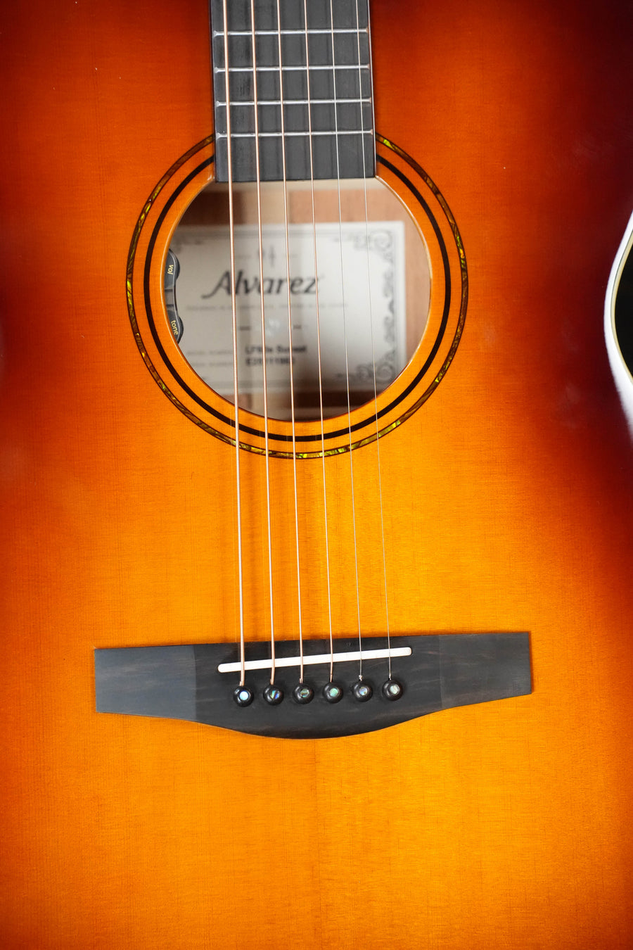 Close-up of the Alvarez Laureate Series LF60e Sunset Sitka/Mahogany OM Guitar, featuring strings, sound hole, bridge, sunburst finish, visible label inside, and enhanced acoustic resonance with an LR Baggs HiFi pickup.