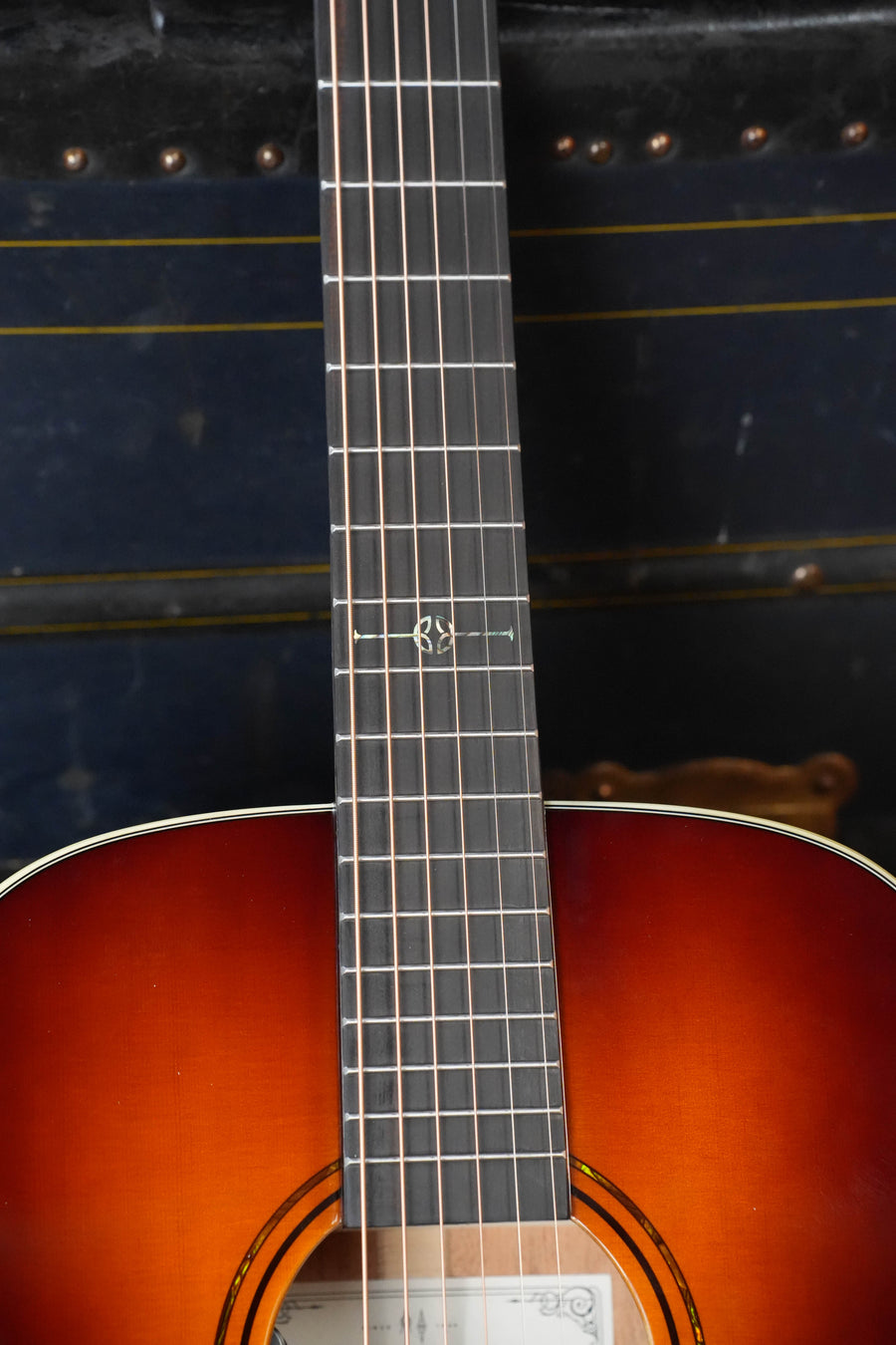 Close-up of the Alvarez Laureate Series LF60e Sunset Sitka/Mahogany OM Guitar showing its neck, fretboard, and sunburst upper body. The dark background highlights the wood grain and LR Baggs HiFi pickup.