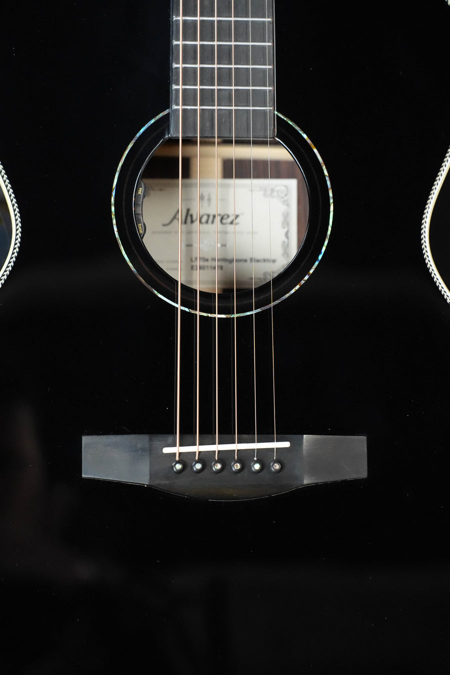 Close-up of an Alvarez Laureate Series LF70e Herringbone Blacktop Sunset OM Guitar (with LR Baggs HiFi pickup) showing the strings, bridge, and sound hole with the Alvarez label visible inside.