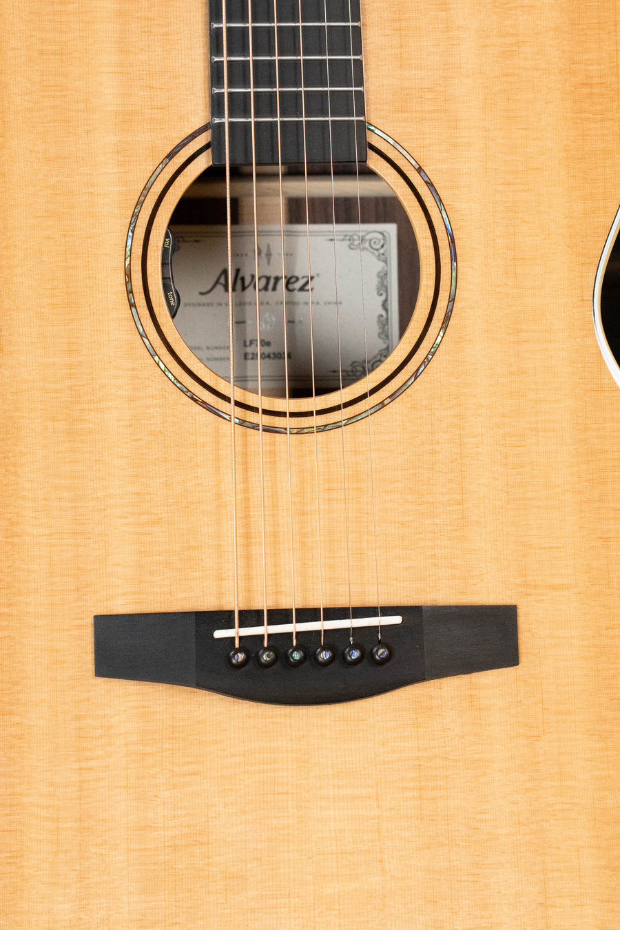 Close-up of the Alvarez Laureate Series LF70e Herringbone Sitka/Rosewood OM (#3036) with LR Baggs Hifi Pickup, showing its six strings, light Sitka spruce top, herringbone binding, and Alvarez label inside the sound hole.