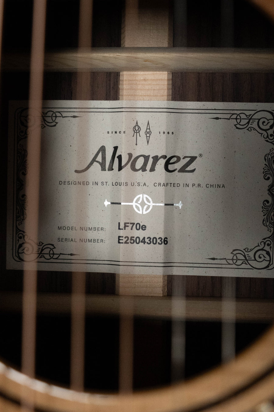 Close-up of the Alvarez Laureate Series LF70e Herringbone Sitka/Rosewood OM w/LR Baggs Hifi Pickup (#3036) label inside the sound hole, showing model and serial details with visible strings and part of the solid Sitka spruce interior.