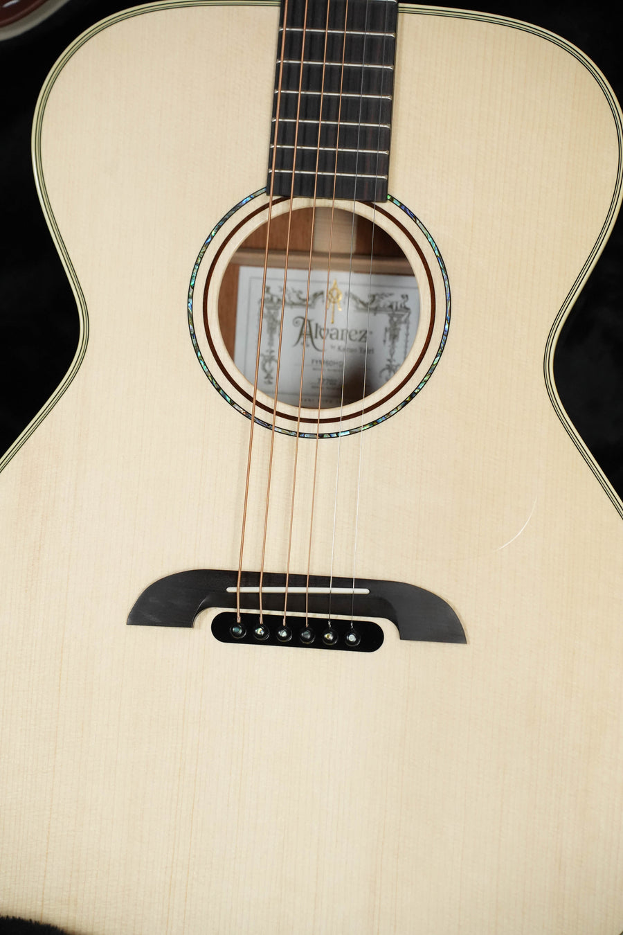 Close-up of the Alvarez Yairi Honduran Series FYM60HD OM Acoustic Guitar #7702, showing soundhole, strings, bridge, and an interior certification label with Alvarez branding, crafted from Adirondack spruce and vintage Honduran mahogany.