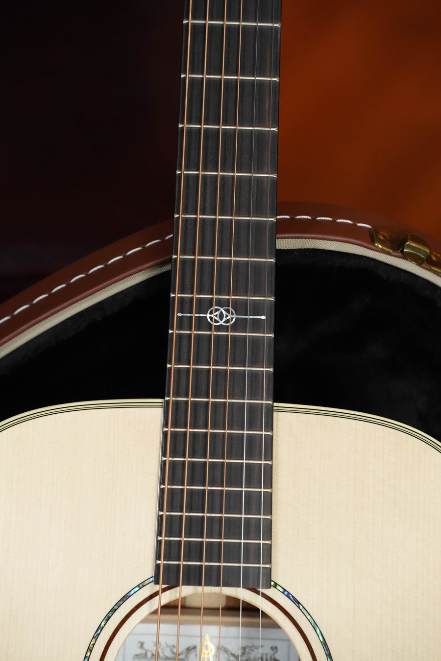 Close-up of an Alvarez Yairi Honduran Series FYM60HD OM Acoustic Guitar #7702 neck and soundhole, showing the detailed wood grain, abalone fretboard inlays, and part of a padded guitar case in the background.