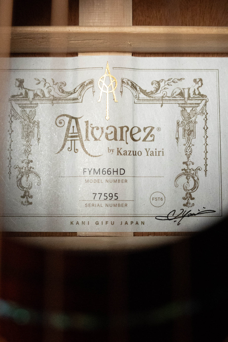 A close-up of the Alvarez Yairi Honduran Series FYM66HD OM Acoustic Guitar #7595 label inside the body, showing decorative designs, Alvarez branding, and a signature.