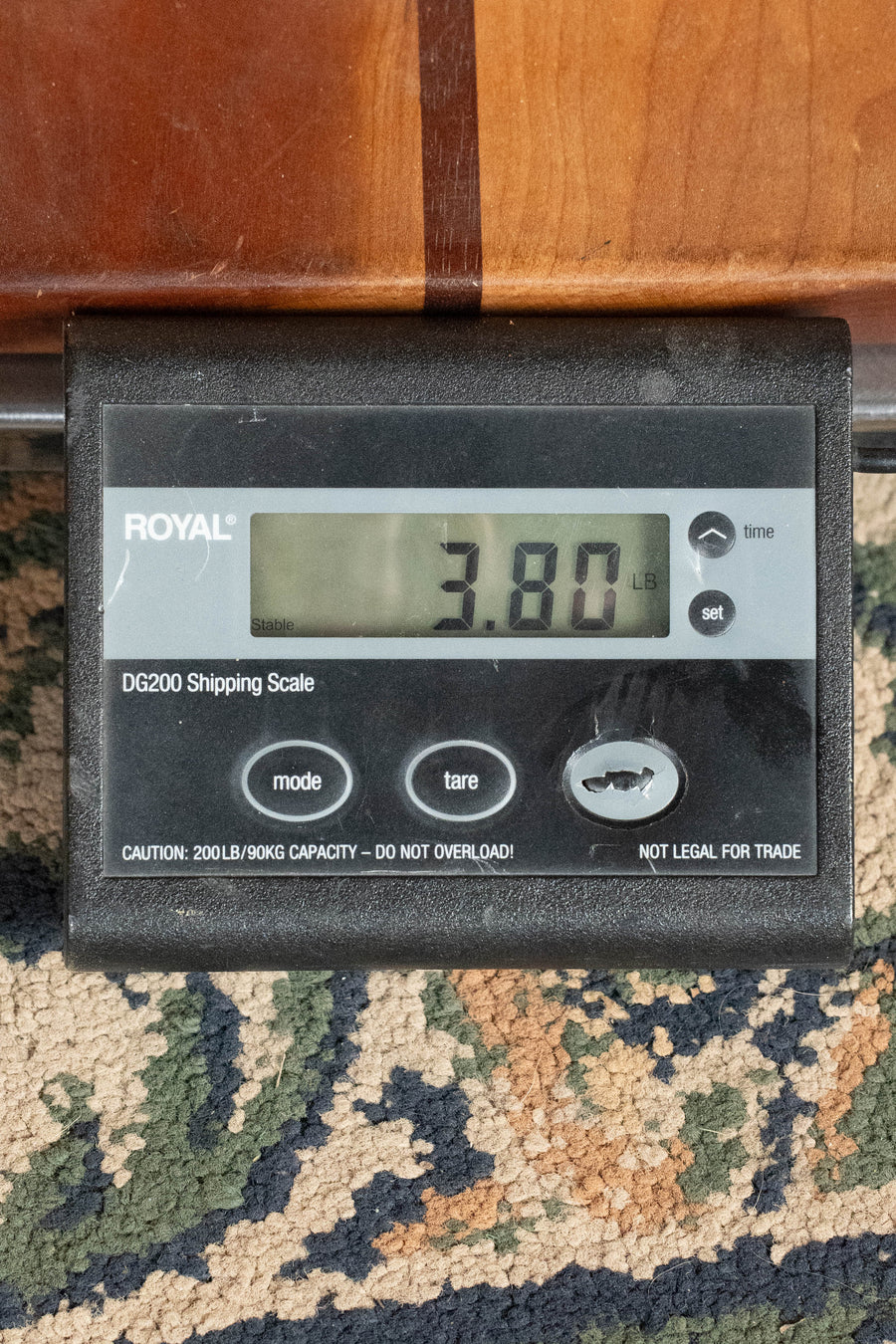 An Alvarez Yairi Honduran Series FYM66HD All Vintage Honduran Mahogany OM Acoustic Guitar (#7595) rests partially on a digital shipping scale, which displays 3.80 pounds with clear labeling, atop a patterned carpet.