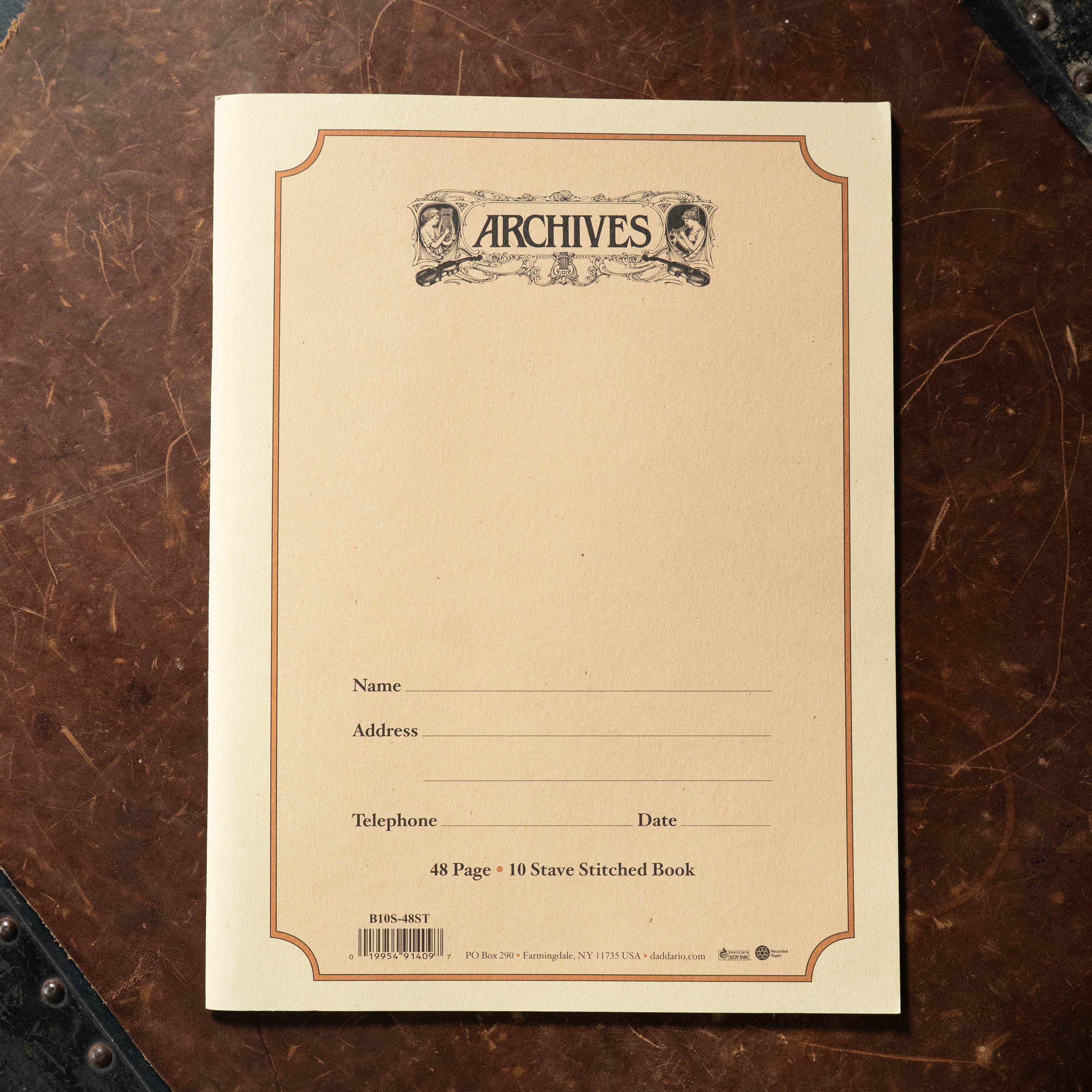 The Acoustic Shoppe’s Archives 48 pg 10 Stave book is cream-colored, measures 9x12, features decorative borders with two illustrated faces, and includes blanks for name, address, telephone, and date.