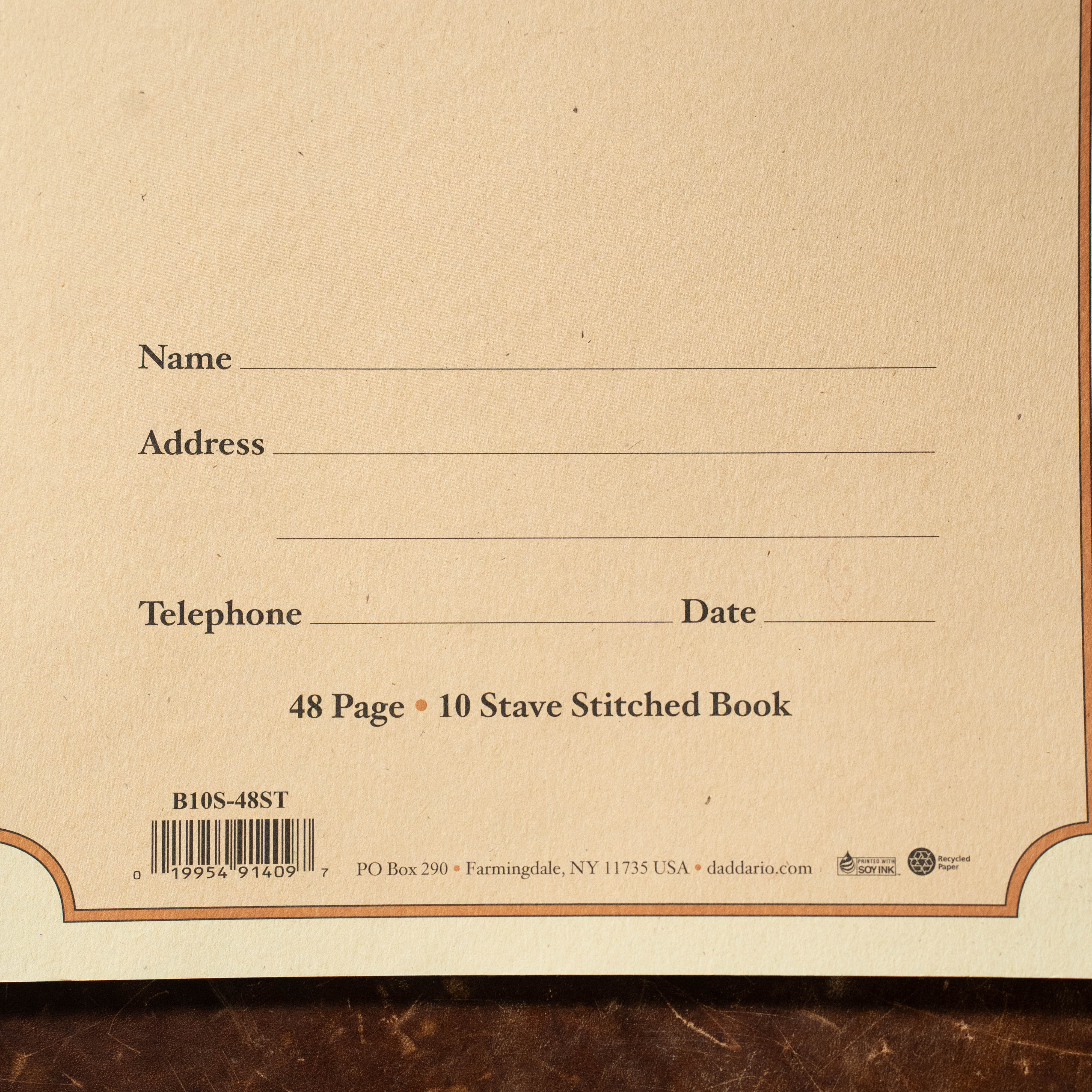 Close-up of The Acoustic Shoppe’s Archives 48 pg 10 Stave book, a 9x12 music manuscript on light brown paper with spaces for personal info. Features “48 Page • 10 Stave Stitched Book” text, barcodes, and publisher details.