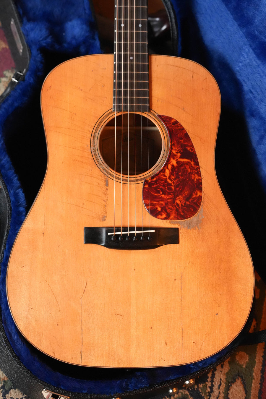 The Atkin Guitars Essential D North American Sitka/Mahogany Acoustic Guitar #4296, with a natural finish and tortoiseshell pickguard, rests in a blue-lined hard case, showing pre-war style wear and visible scratches.