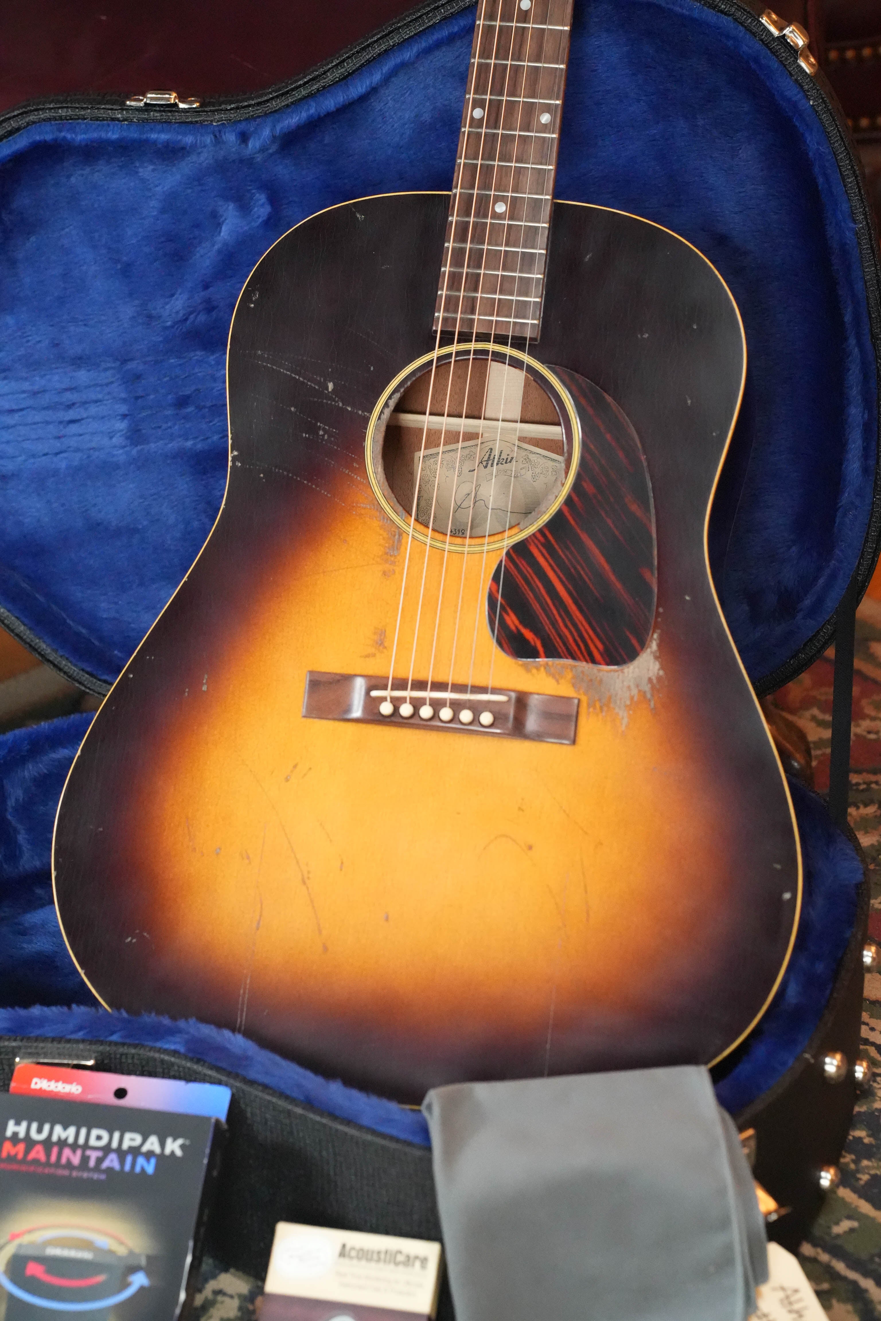 An Atkin Guitars J43 45MM Baked Sitka/Mahogany Heavy Aged Slope Shoulder Dreadnought #4398 sits in its open blue-lined case, with a Humidipak Maintain pack and guitar care items displayed in front.
