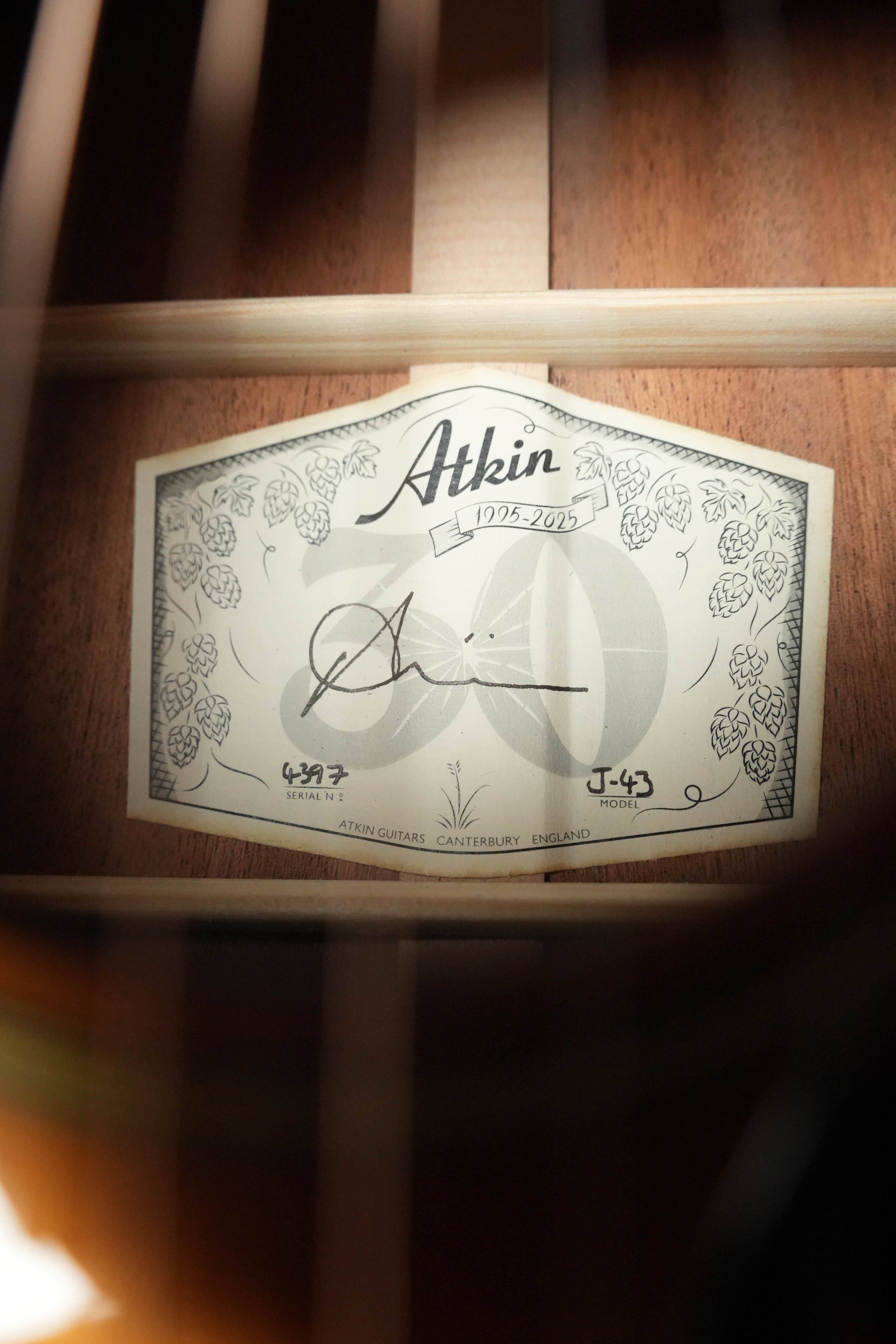 A close-up of the label inside an Atkin Guitars J43 Baked Sitka/Mahogany Heavy Aged Slope Shoulder Dreadnought Acoustic Guitar #4397, showing decorative hops, signatures, reference numbers, and wooden braces in the background.