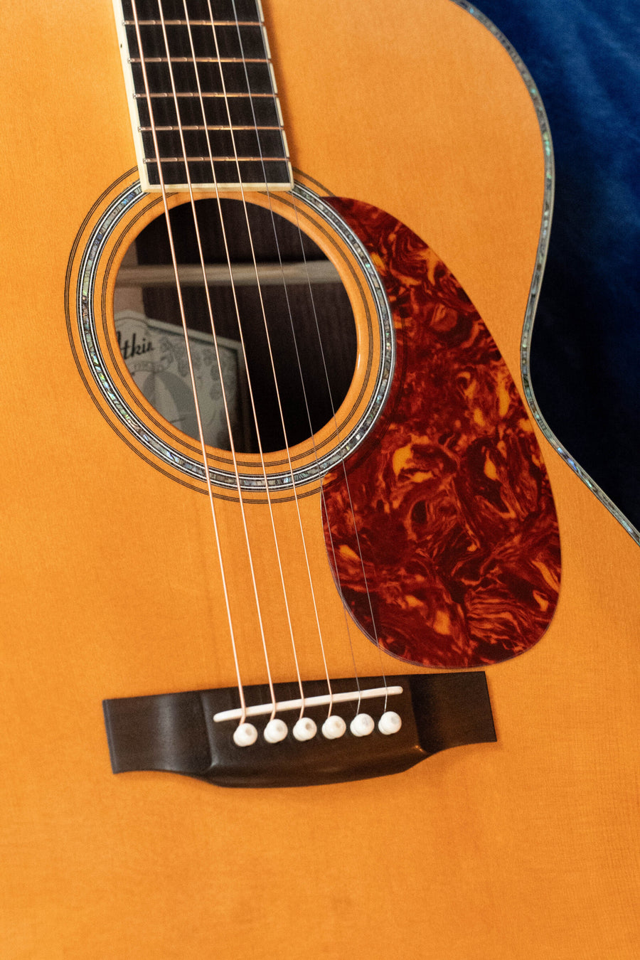 Close-up of an Atkin Guitars 00037 DLX Sitka/East Indian Rosewood OOO Acoustic Guitar #3895, highlighting the strings, bridge, soundhole, tortoiseshell-pattern pickguard, and the wood grain of the body. The aged nitrocellulose finish accentuates its classic aesthetic reminiscent of a pre-war triple-0 guitar.