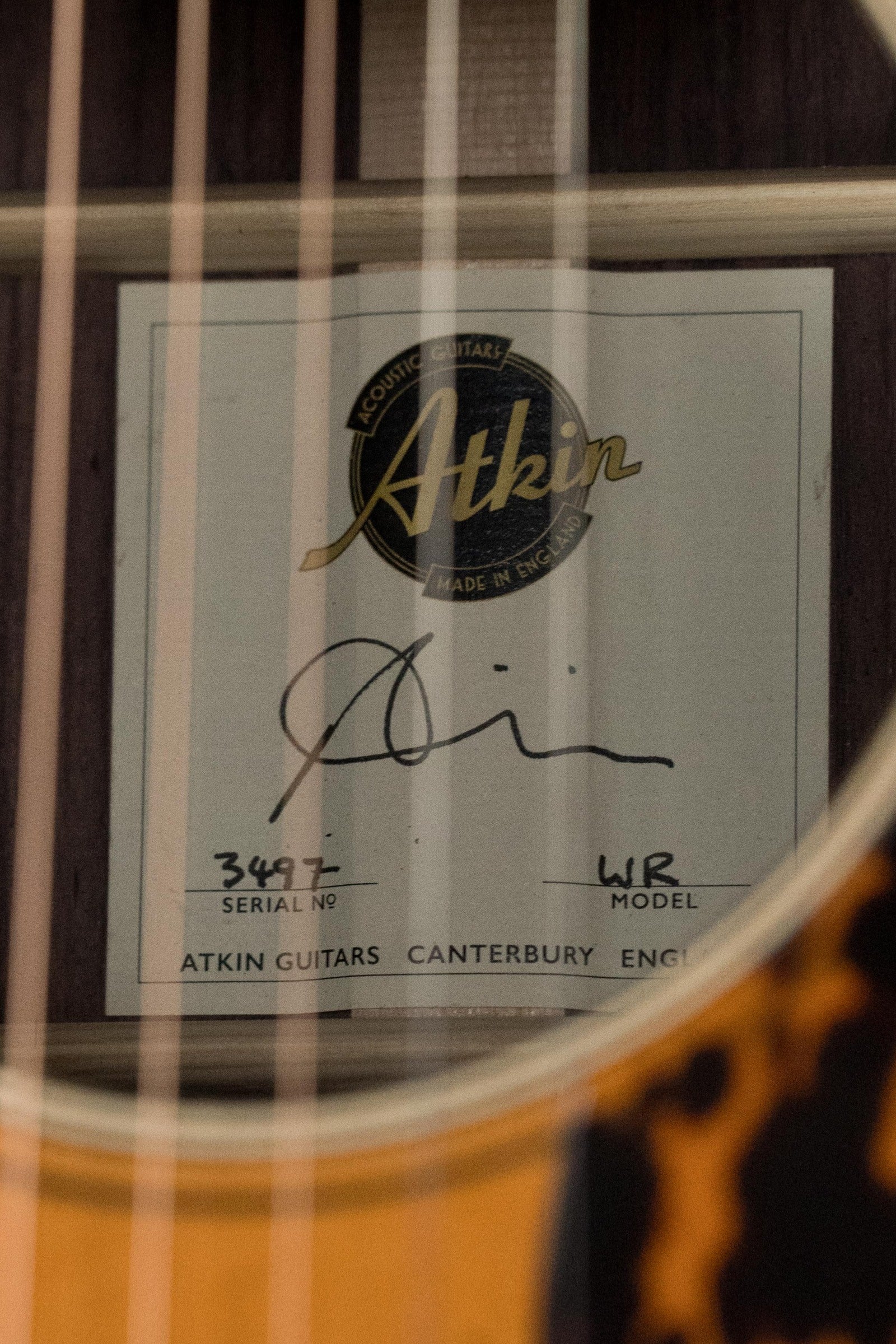 Close-up of the label inside an Atkin Guitars White Rice Baked Sitka/Rosewood Dreadnought Acoustic Guitar #3497, showing the logo, signature, serial number, and Canterbury England text through the rosewood strings.
