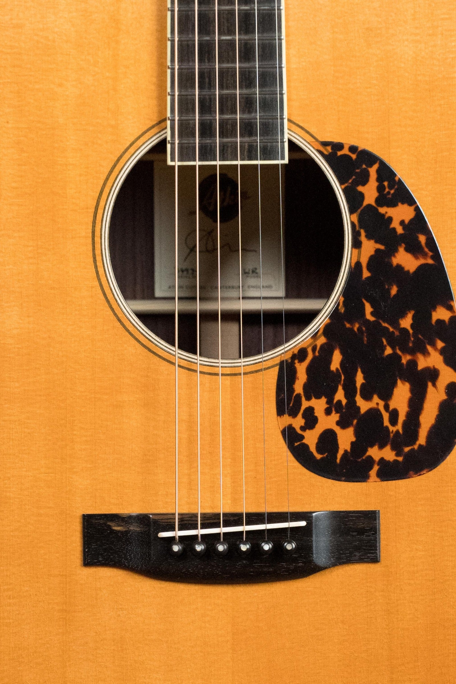 Close-up of the Atkin Guitars White Rice Baked Sitka/Rosewood Dreadnought Acoustic Guitar #3497, featuring its sound hole, strings, bridge, and tortoiseshell-patterned pickguard set against a light wood body—delivering classic vintage tone.