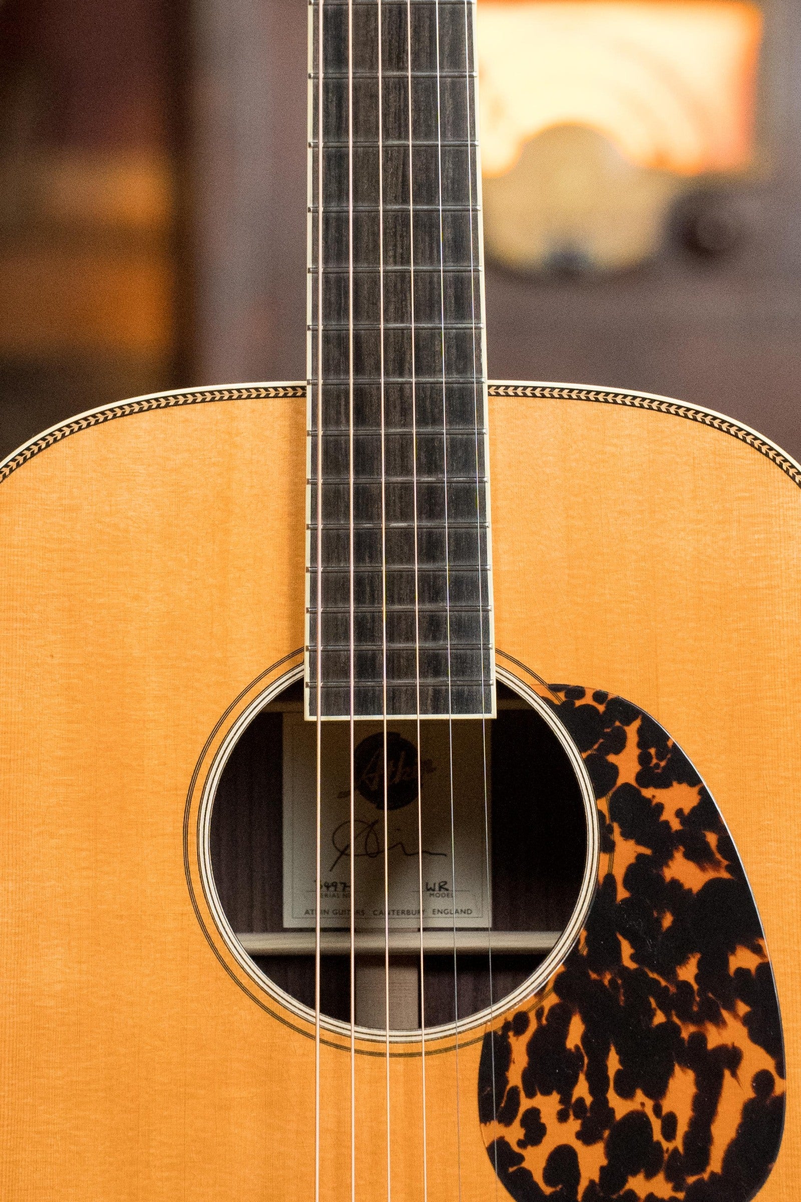 Close-up of an Atkin Guitars White Rice Baked Sitka/Rosewood Dreadnought Acoustic Guitar #3497, showing strings, sound hole, tortoiseshell pickguard, and signed label. Indian rosewood back and sides hint at its vintage tone. Blurred background.