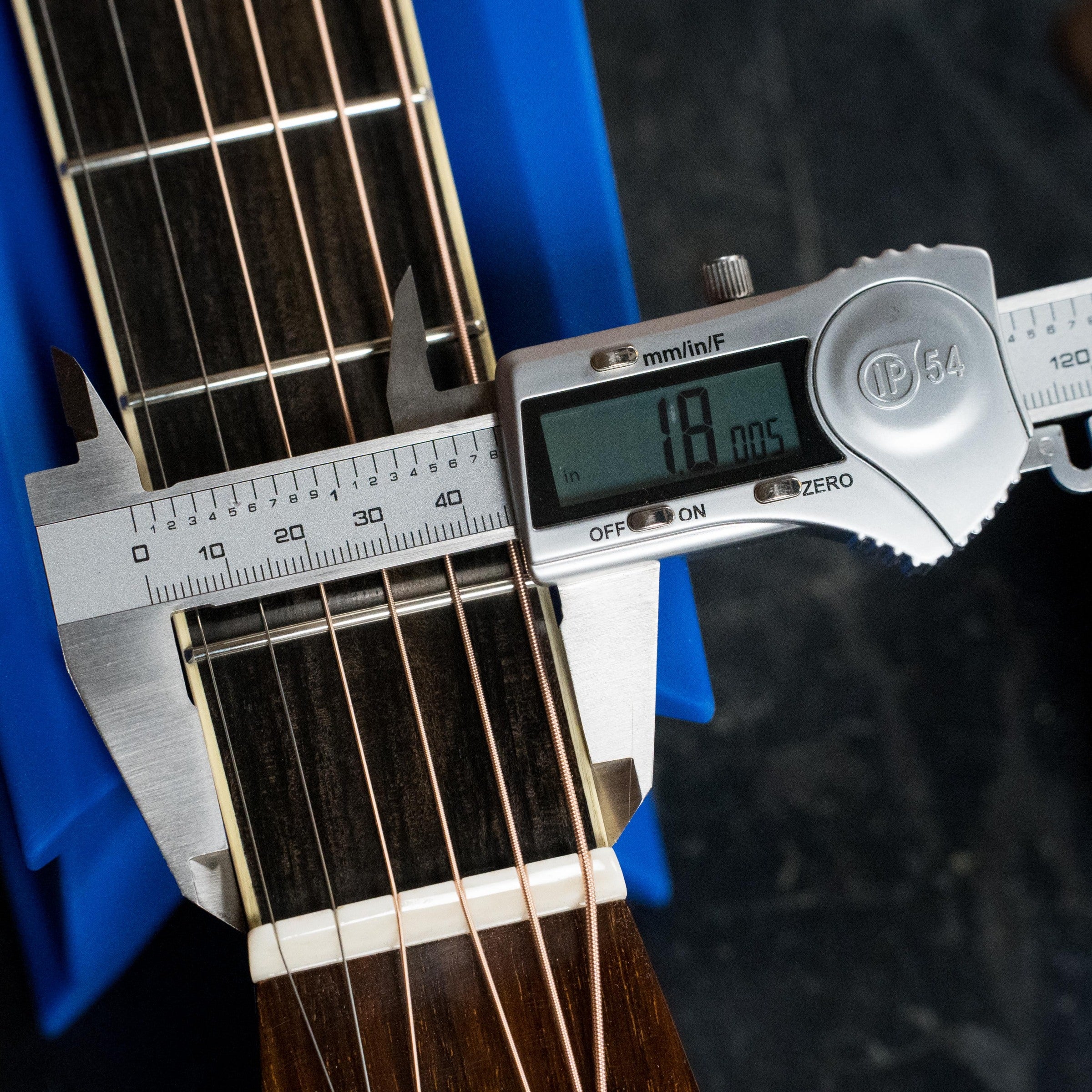 A digital caliper shows the nut width of an Atkin Guitars White Rice Baked Sitka/Rosewood Dreadnought Acoustic Guitar #3497 as 18.0 mm, with the vintage-tone guitar held in place by a blue support.