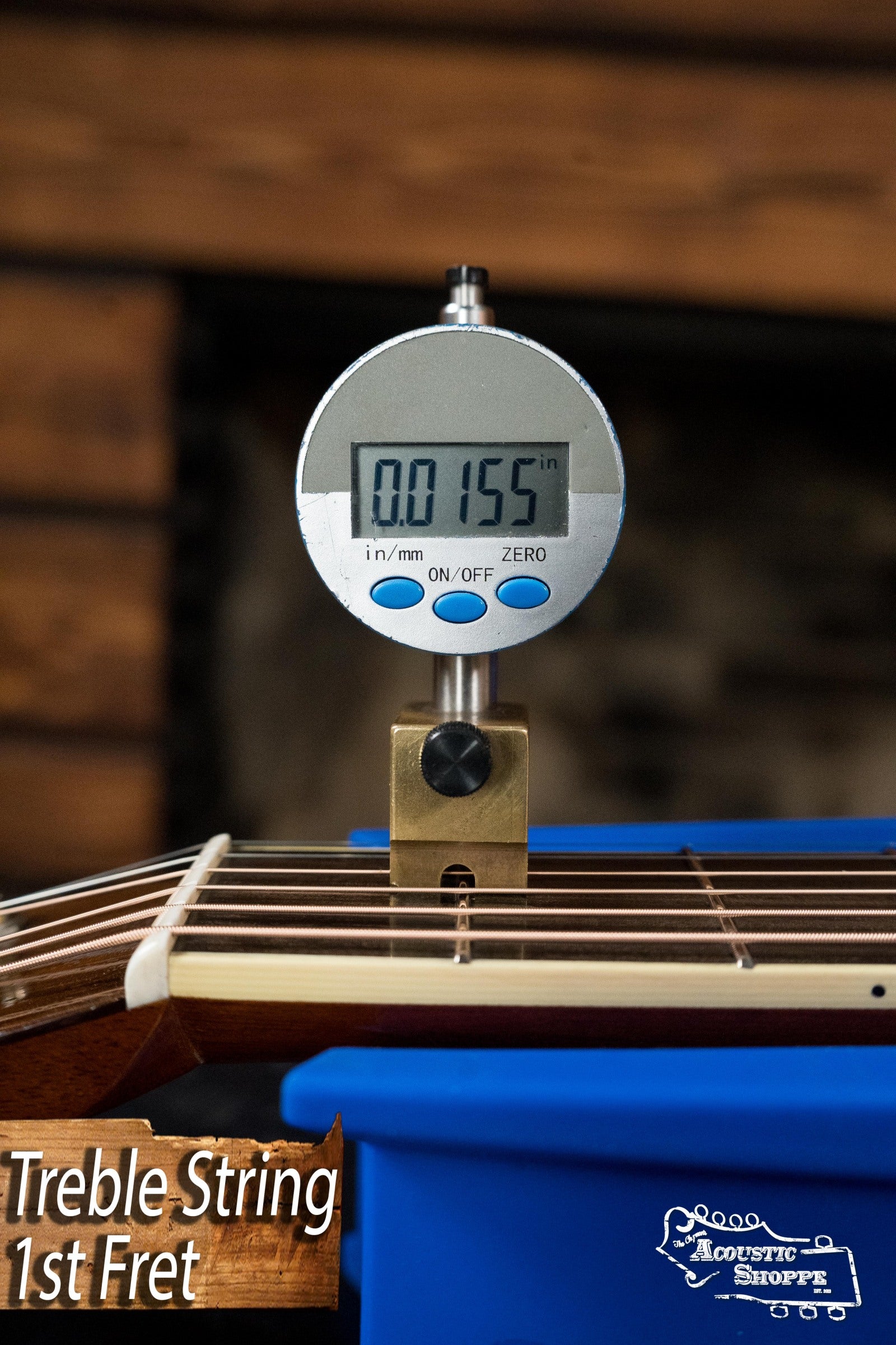 A digital caliper reads 0.0155 inches while measuring the treble string height at the 1st fret on an Atkin Guitars White Rice Baked Sitka/Rosewood Dreadnought Acoustic Guitar #3497; “Treble String 1st Fret” and Acoustic Shoppe logo are shown.