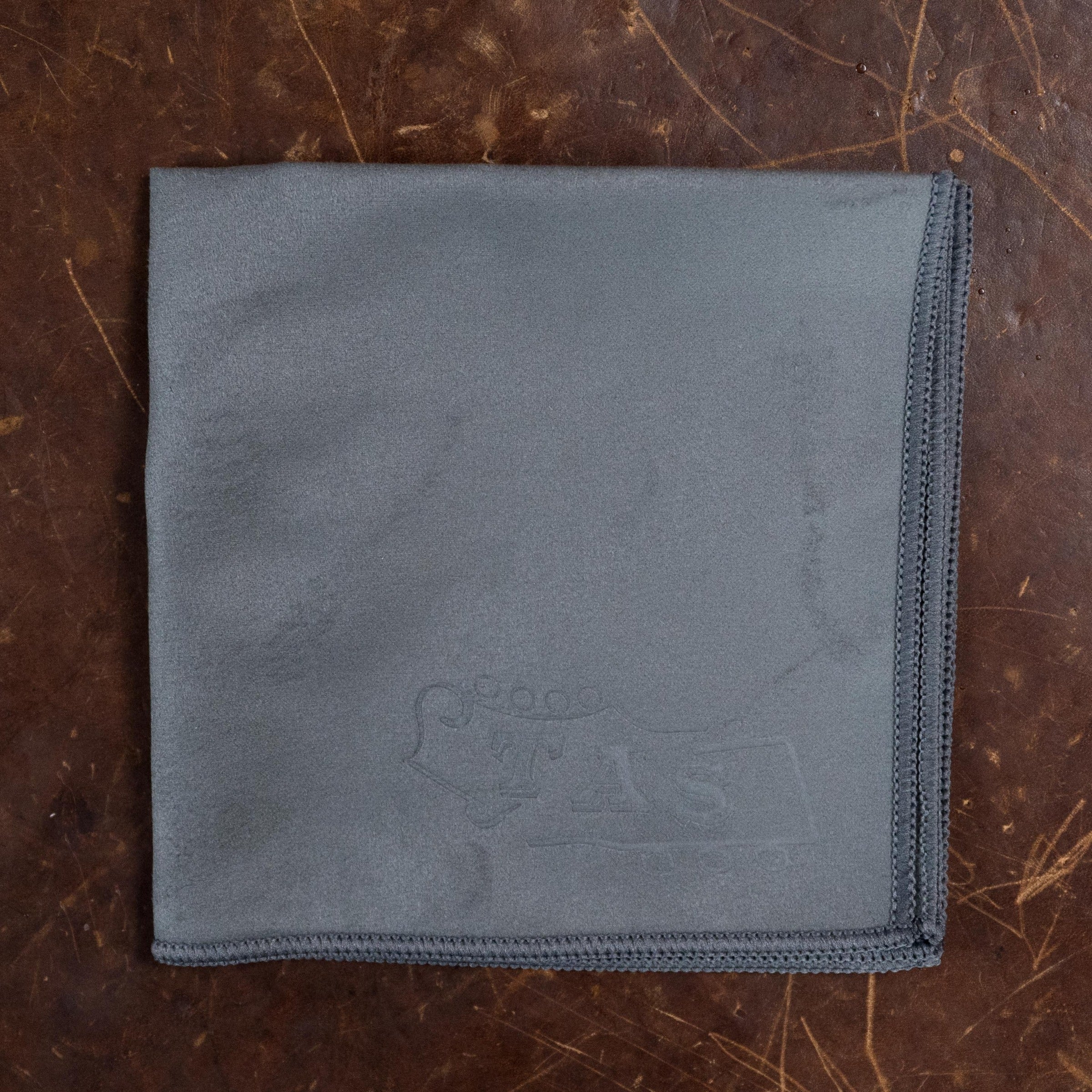 A folded gray microfiber cloth with stitched edges rests on the textured surface of an Atkin Guitars White Rice Baked Sitka/Rosewood Dreadnought Acoustic Guitar #3497, with a subtle embossed design near one corner of the cloth.