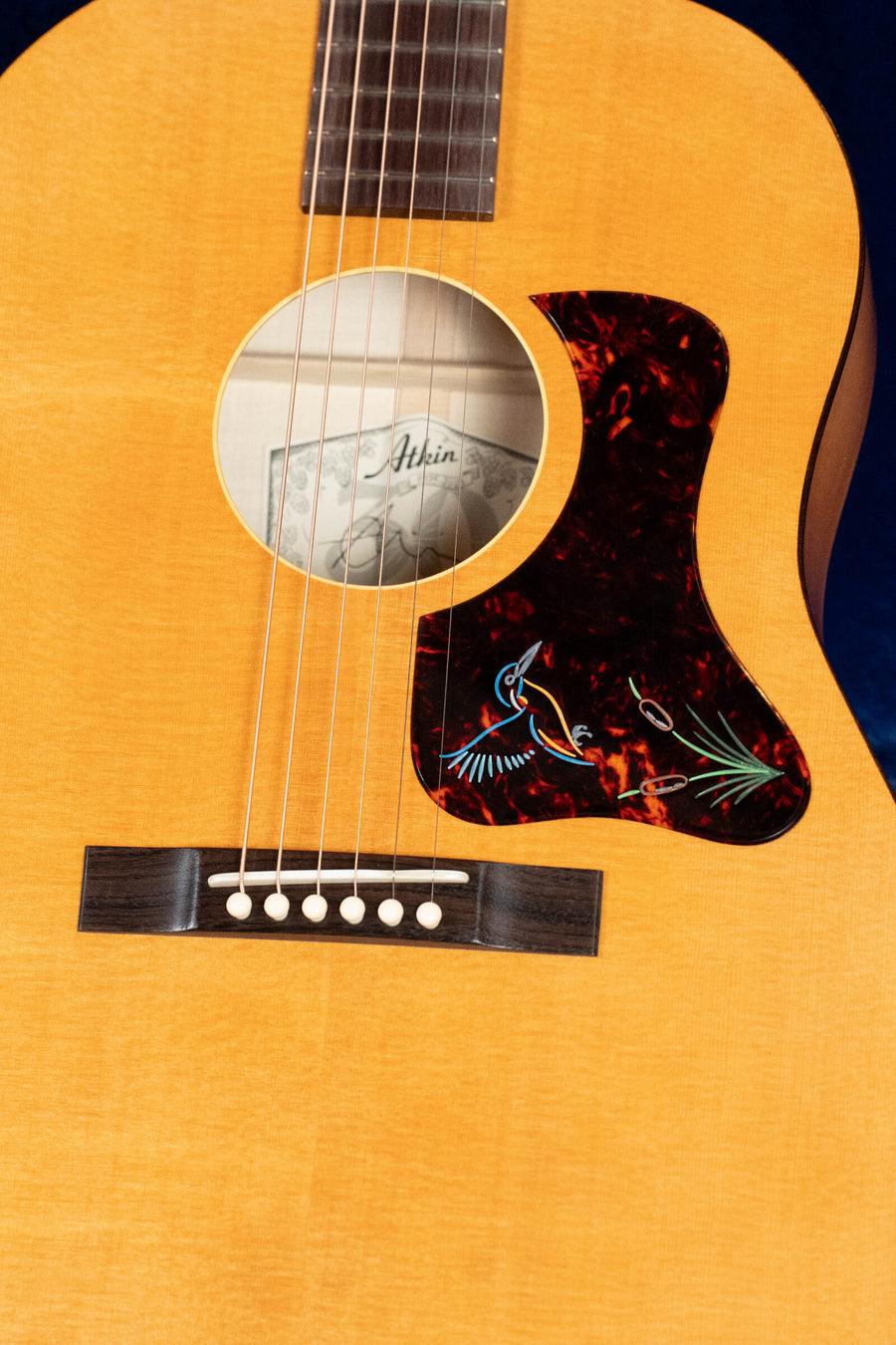 Close-up of the Atkin Guitars Atkin 19 Kingfisher Sitka/Maple Dreadnought Acoustic Guitar #3892, showing its Sitka spruce top, six strings, dark wood bridge with white pins, round sound hole, and decorative bird-inlay pickguard.
