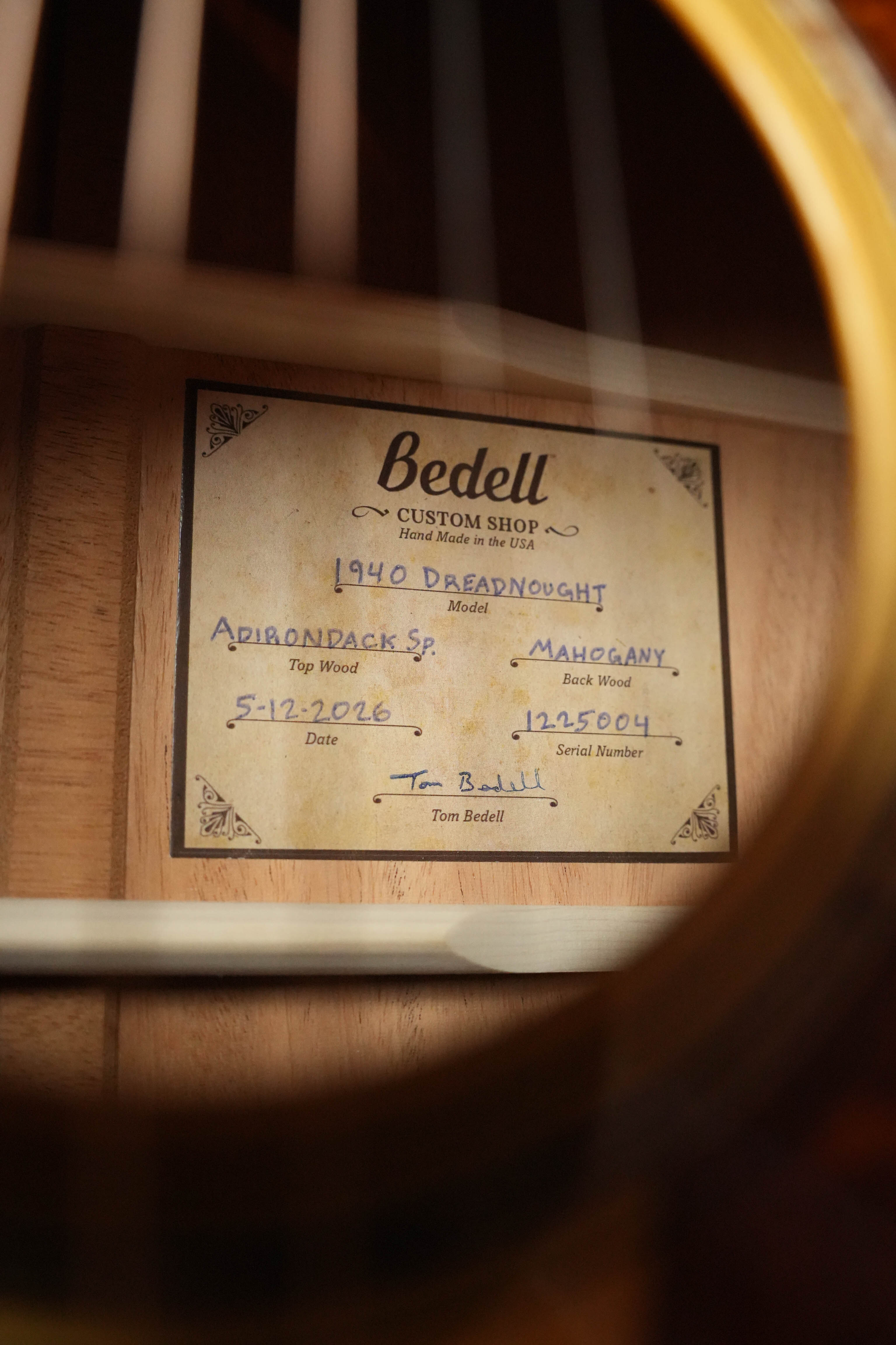 Close-up of a label inside a Bedell Guitars Special Edition 1940 Dreadnought Narrow Nut Acoustic Guitar #5004, with Tom Bedell visible through the strings and model details including top, back, date, and serial number.