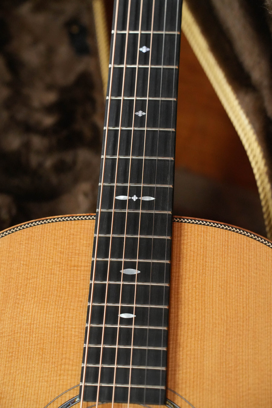 Close-up of the Boucher HG-56-M Adirondack/Rosewood OOO Acoustic Guitar #1370 from The Acoustic Shoppe, highlighting its strings, frets, and diamond inlays on a dark fretboard. Expertly crafted, it rests in a plush-lined case.
