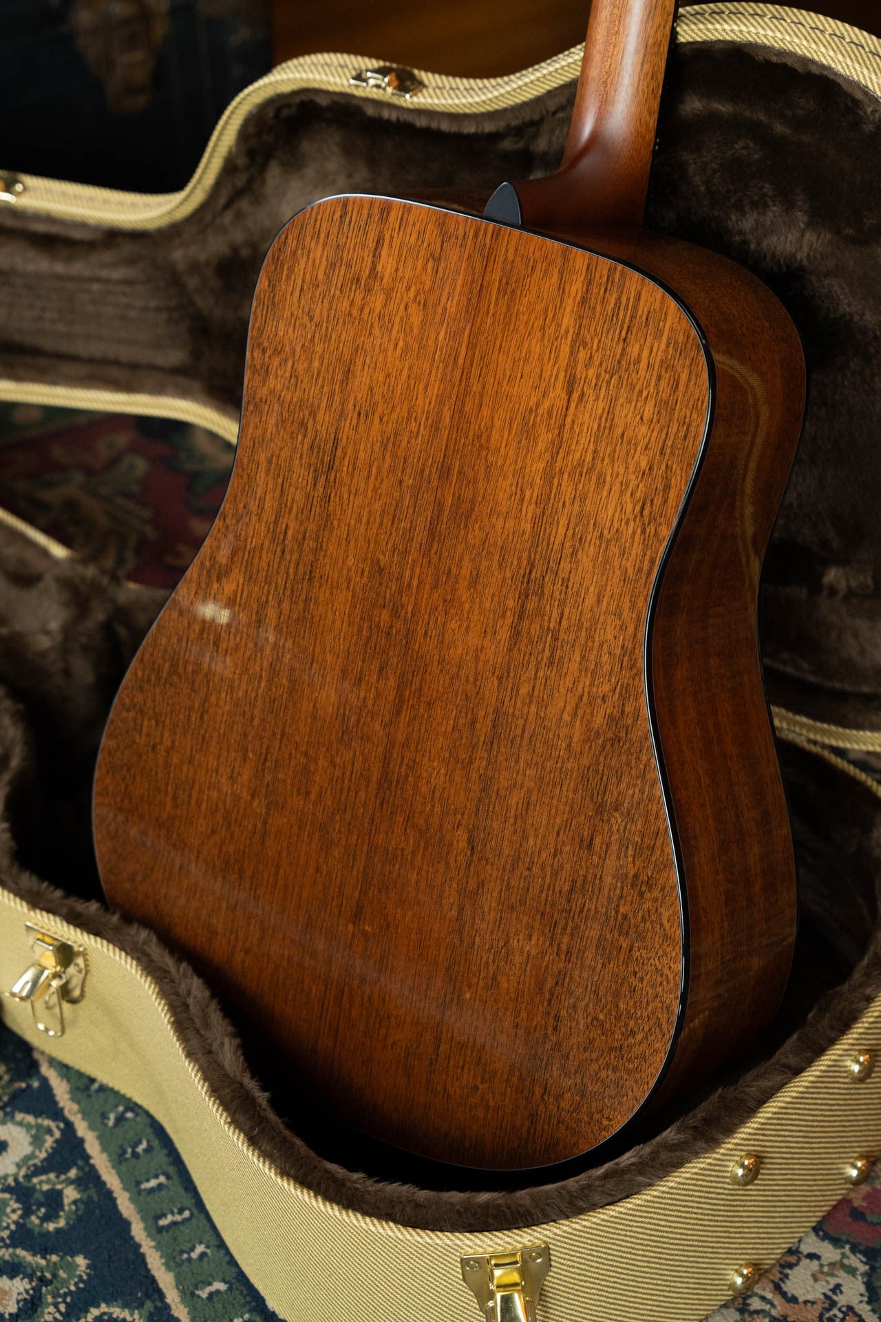 A close-up of the back of a Boucher Guitars BG-42T-G Bluegrass Goose Series Torrefied Master Grade Adirondack/Mahogany Dreadnought Gold Pack Acoustic Guitar #1035, resting in a plush-lined case on a patterned rug.